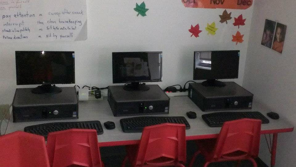Three computer workstations with monitors, keyboards, and red chairs