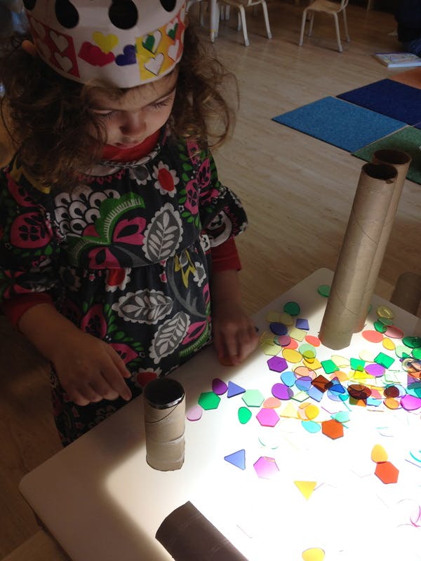 Child playing with colorful shapes and cardboard tubes on a light table