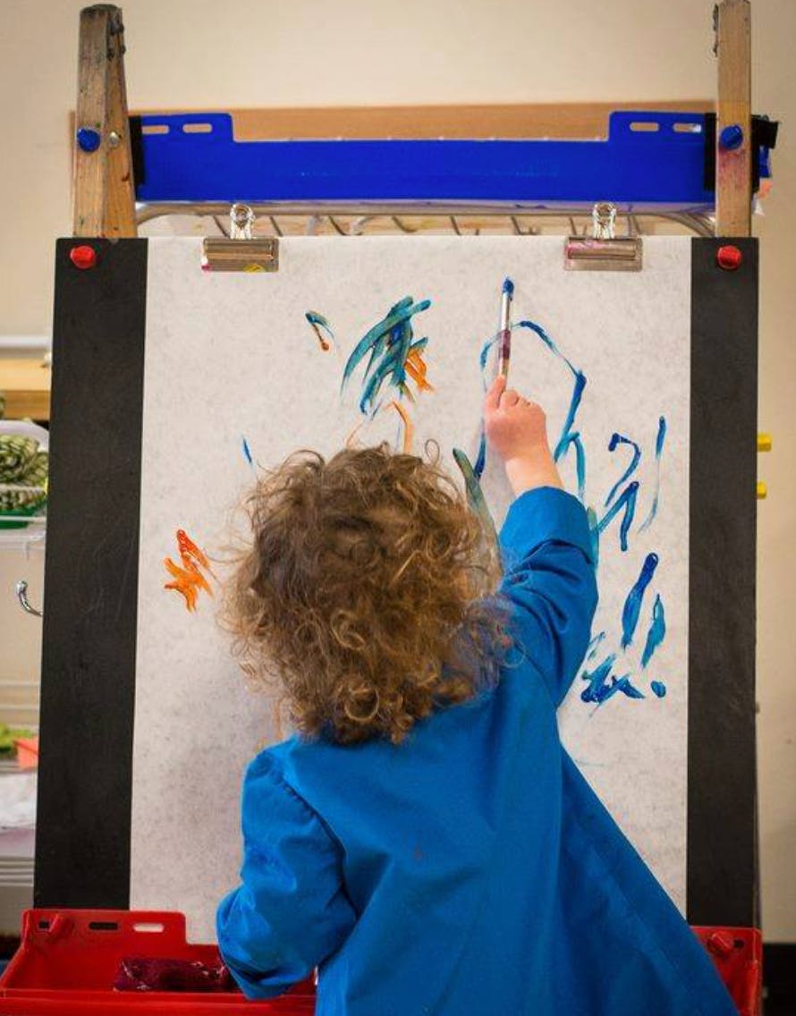 Child in blue smock painting on an easel