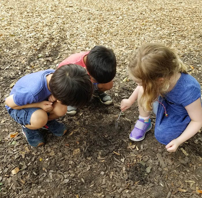Three children crouching and digging in dirt