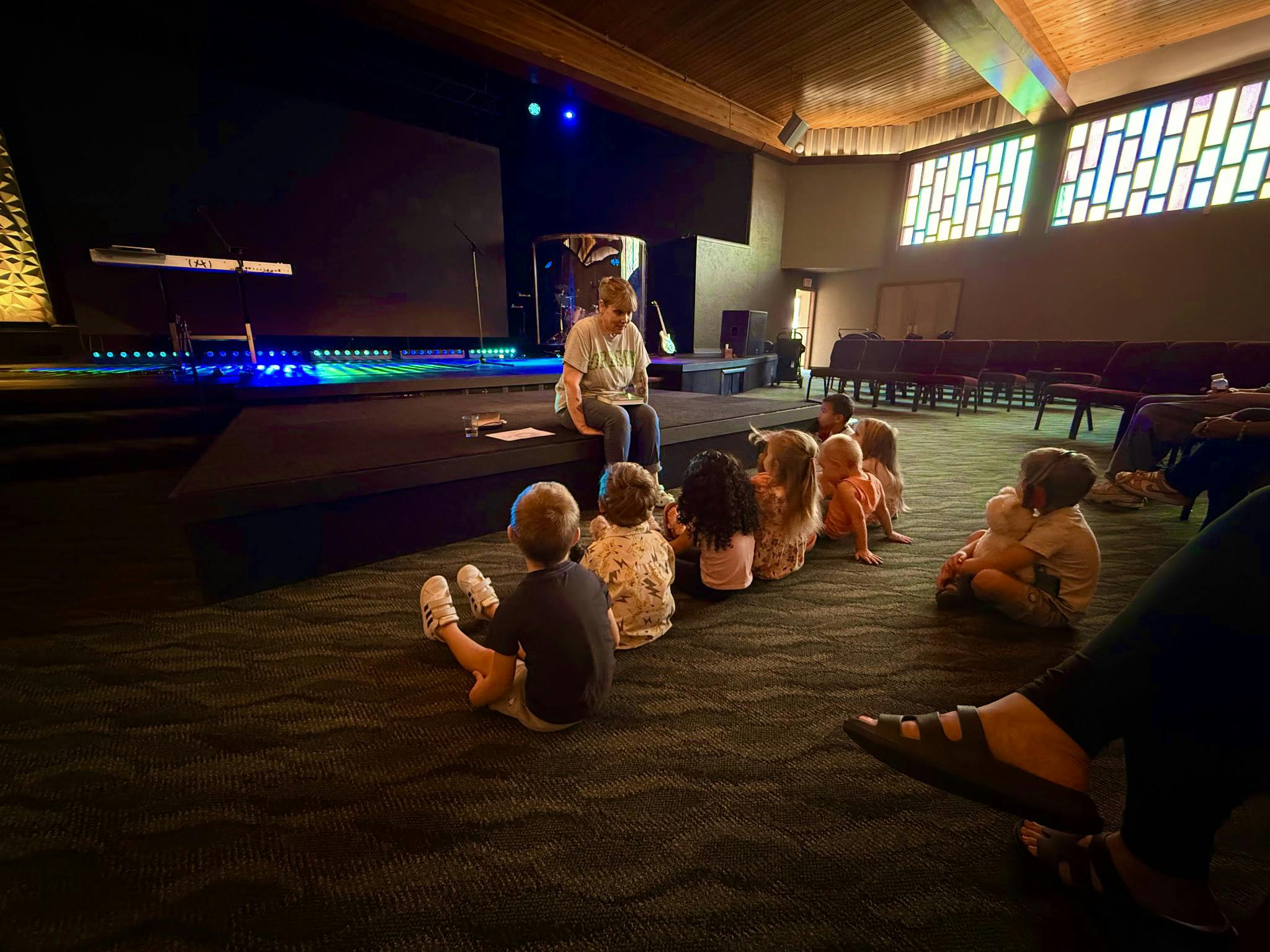 Adult sitting on a stage reading to a group of children sitting on the floor
