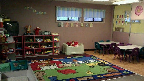Playroom with a colorful rug, toy shelves, and small tables with chairs