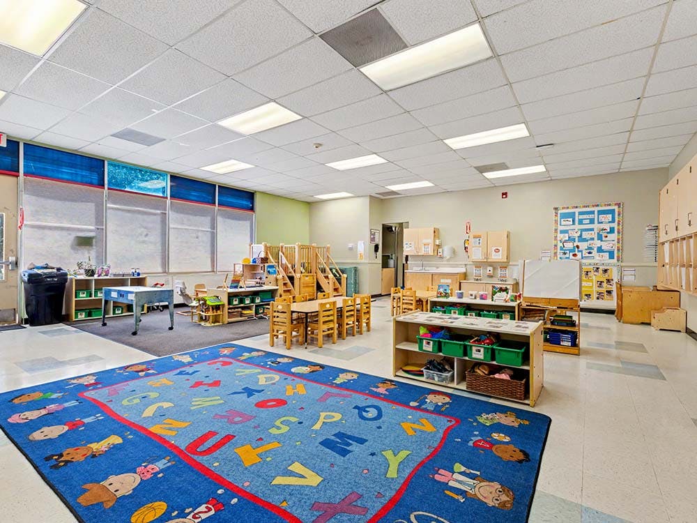 Empty classroom with small tables, chairs, and play equipment