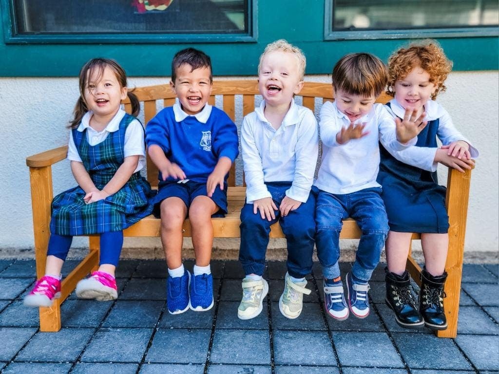 Five young children sitting on a wooden bench outdoors