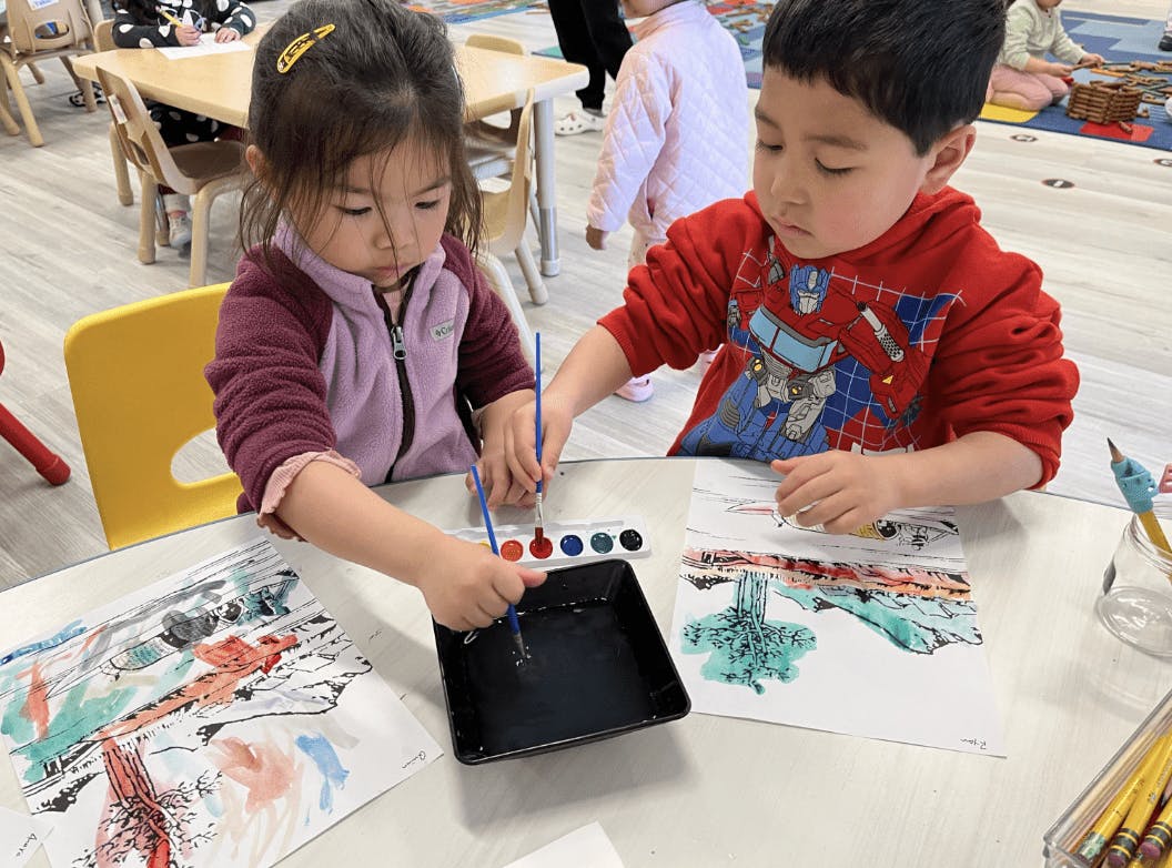 Two children painting with watercolors at a table