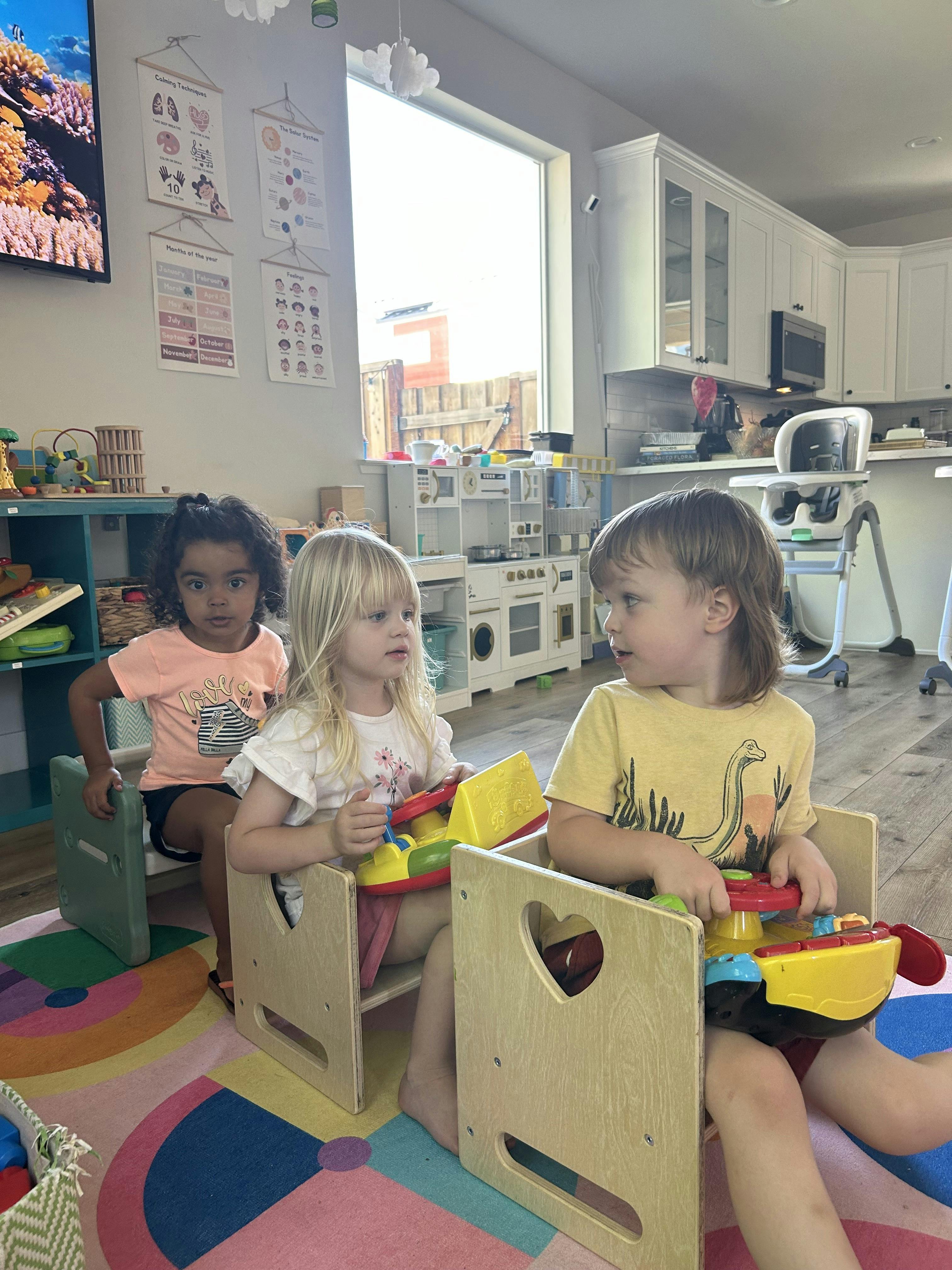 Three children sitting in small chairs playing with toys in a room