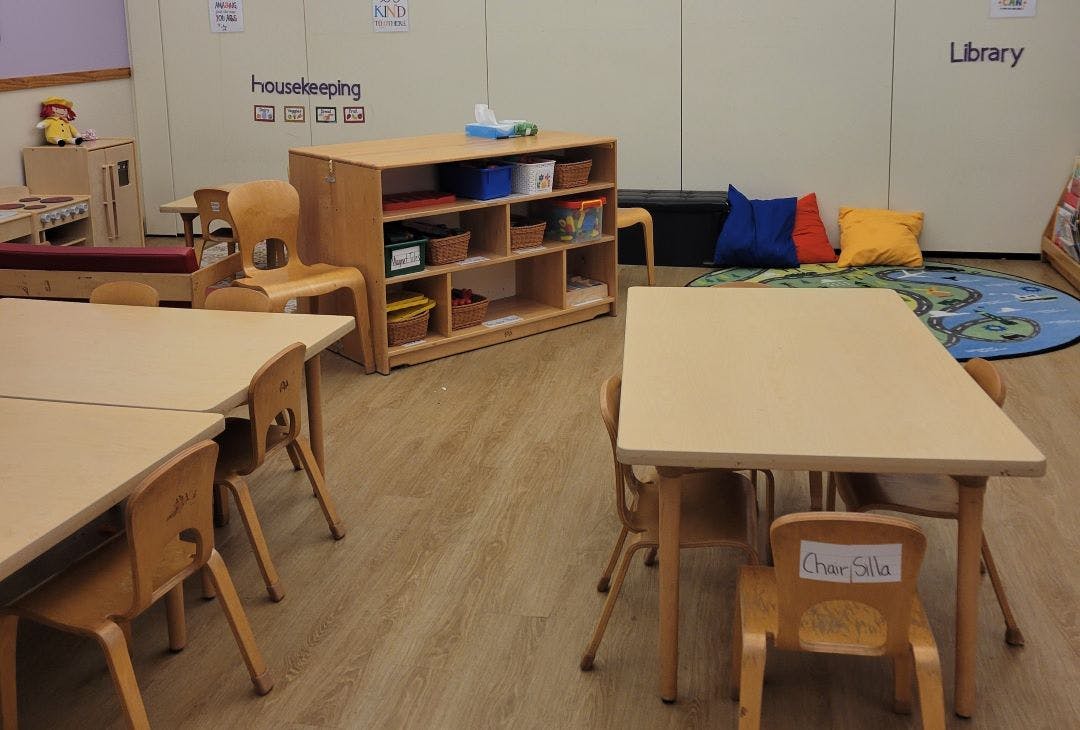 children's classroom with small tables and chairs, a shelving unit, and reading corner