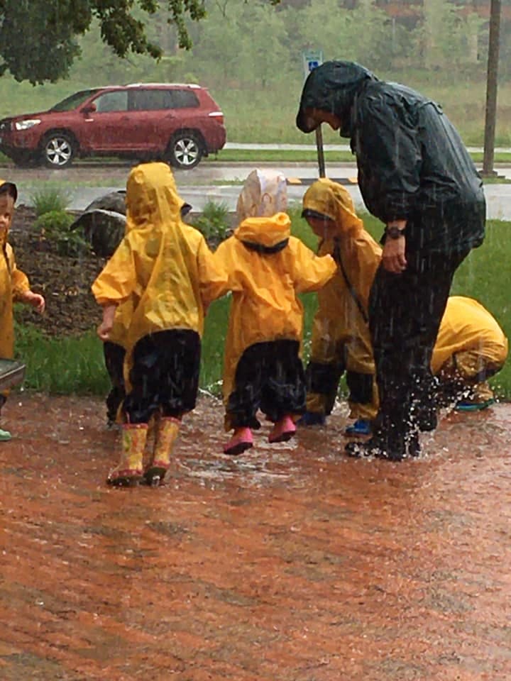 Person and children in rain gear playing in puddles during rain