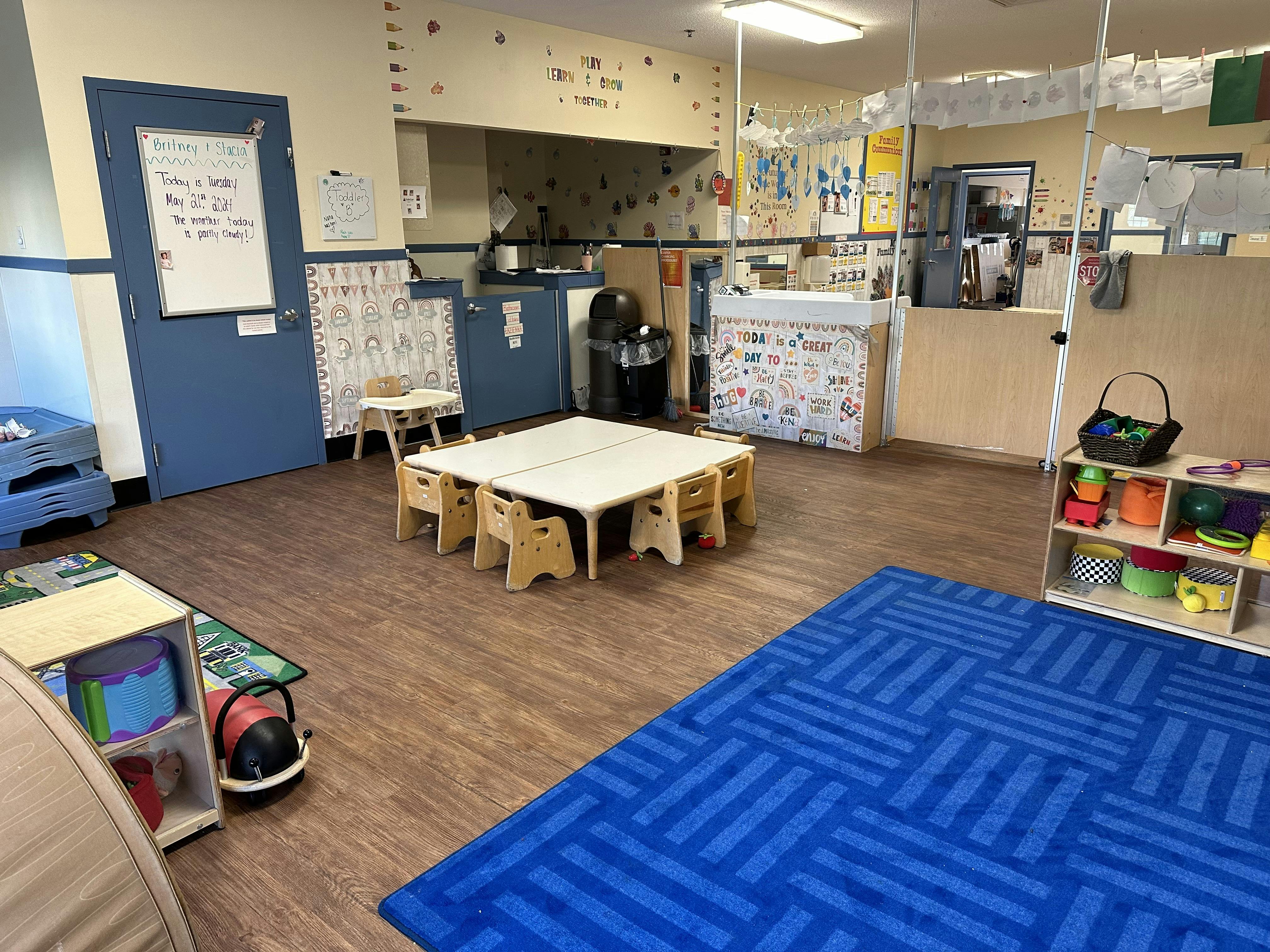 A colorful childcare classroom with small tables and chairs, toys, and decorations