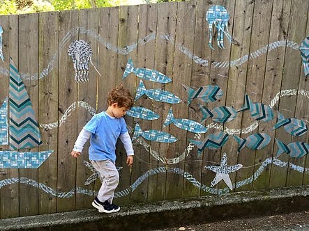 Child walking along a ledge next to a fence with painted sea creatures