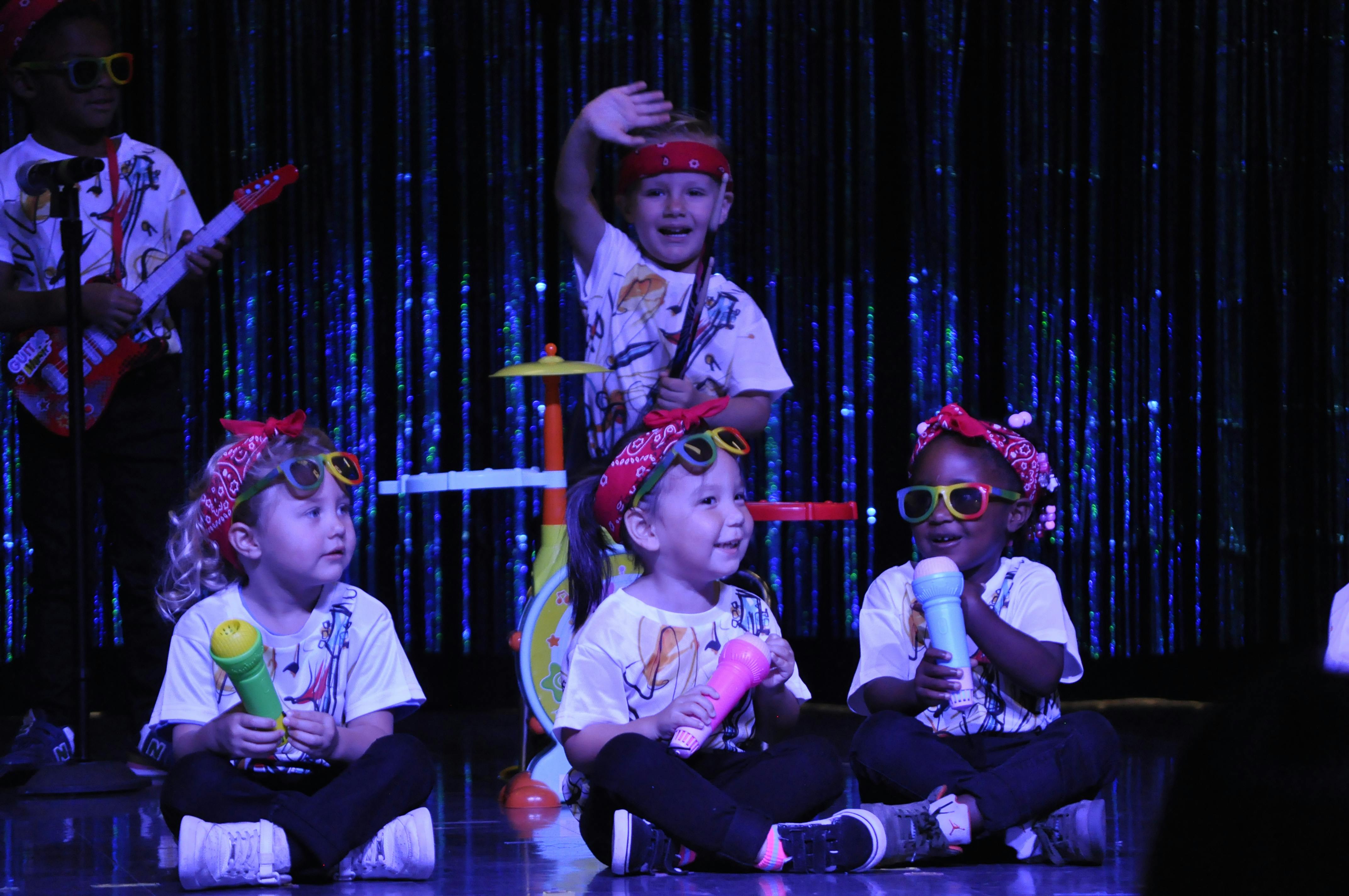 Children performing on stage with toy instruments