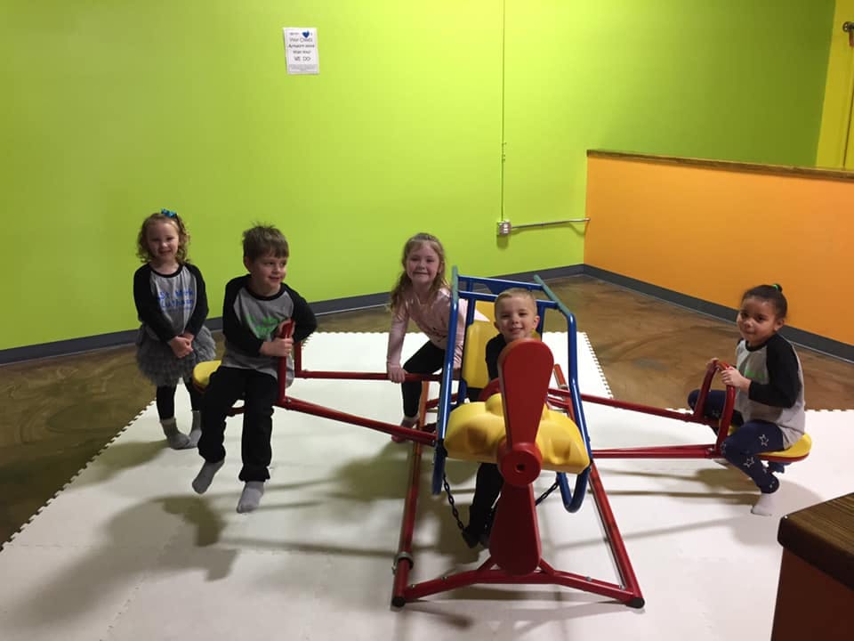 Four children playing on a seesaw in an indoor play area