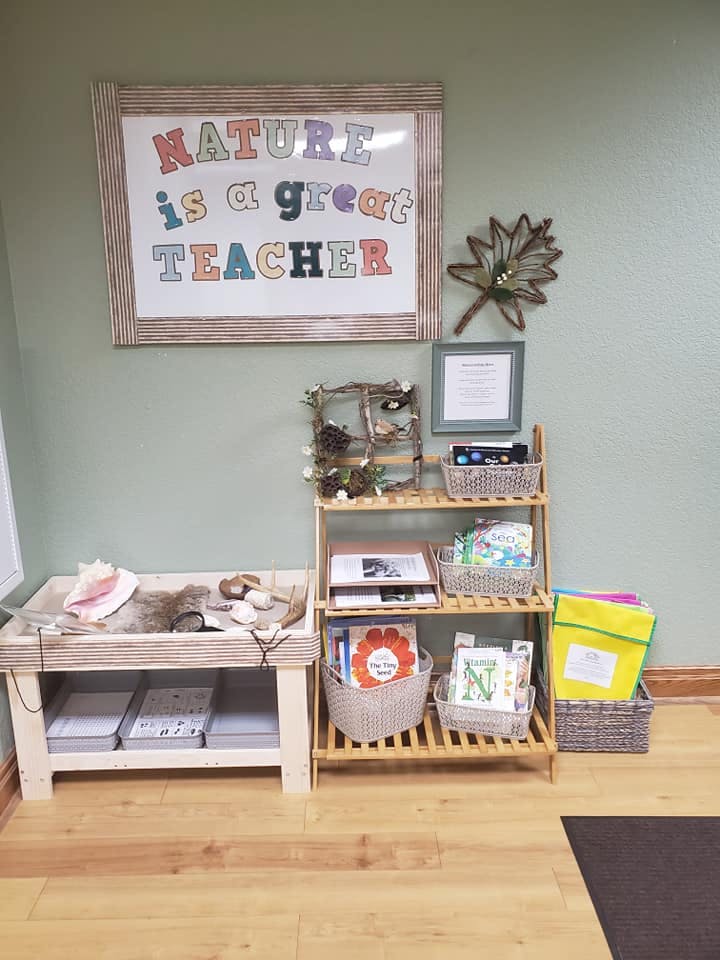 Classroom display with "Nature is a great teacher" sign, shelves with books and baskets