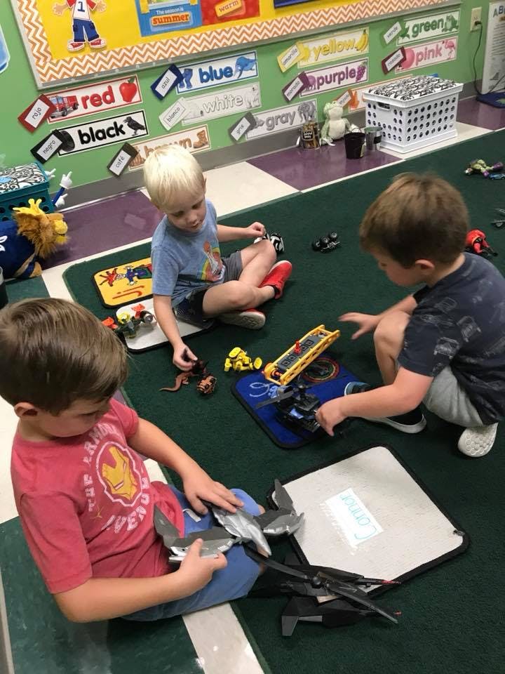Three children playing with toys on a green rug in a classroom