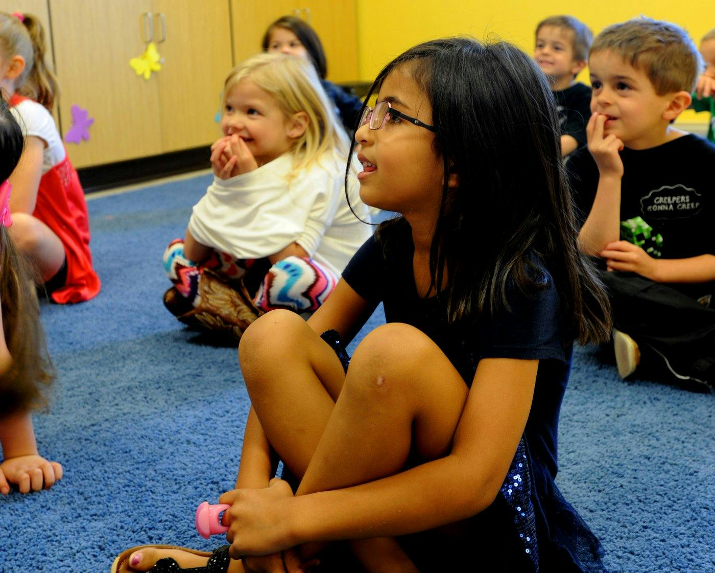 Children sitting on a blue carpet in a classroom