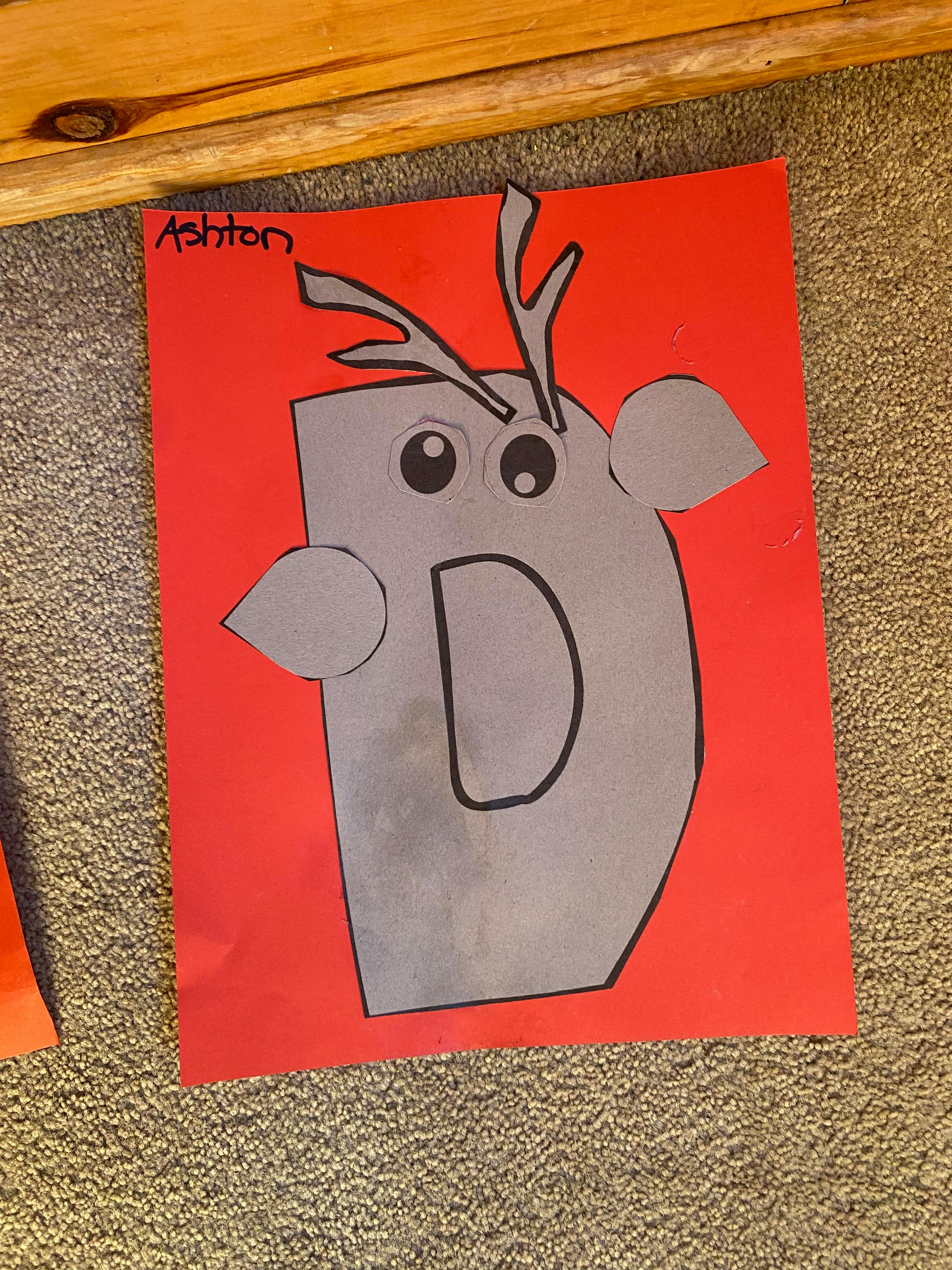 Paper craft of a letter D with antlers and eyes on a red background