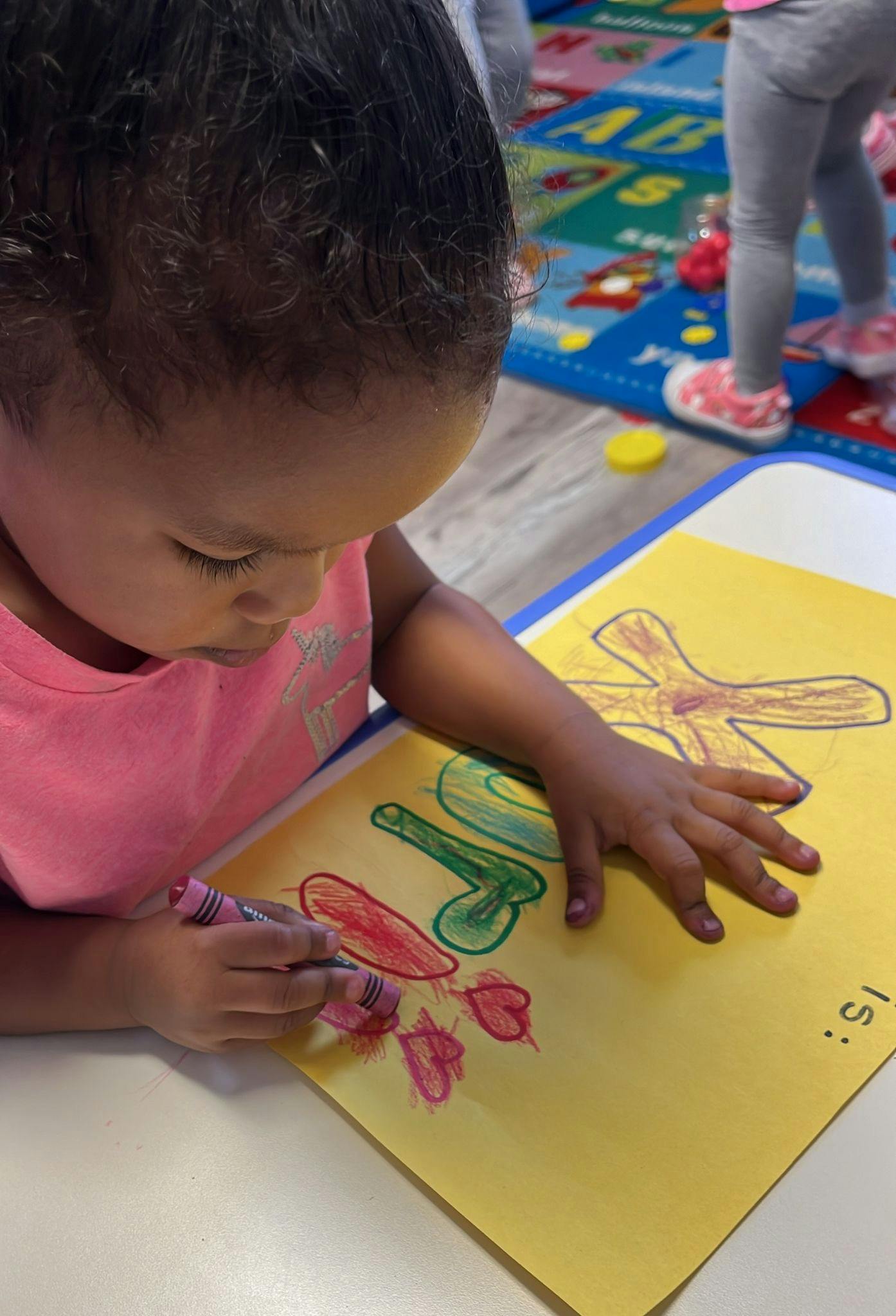 Child coloring on yellow paper with crayons