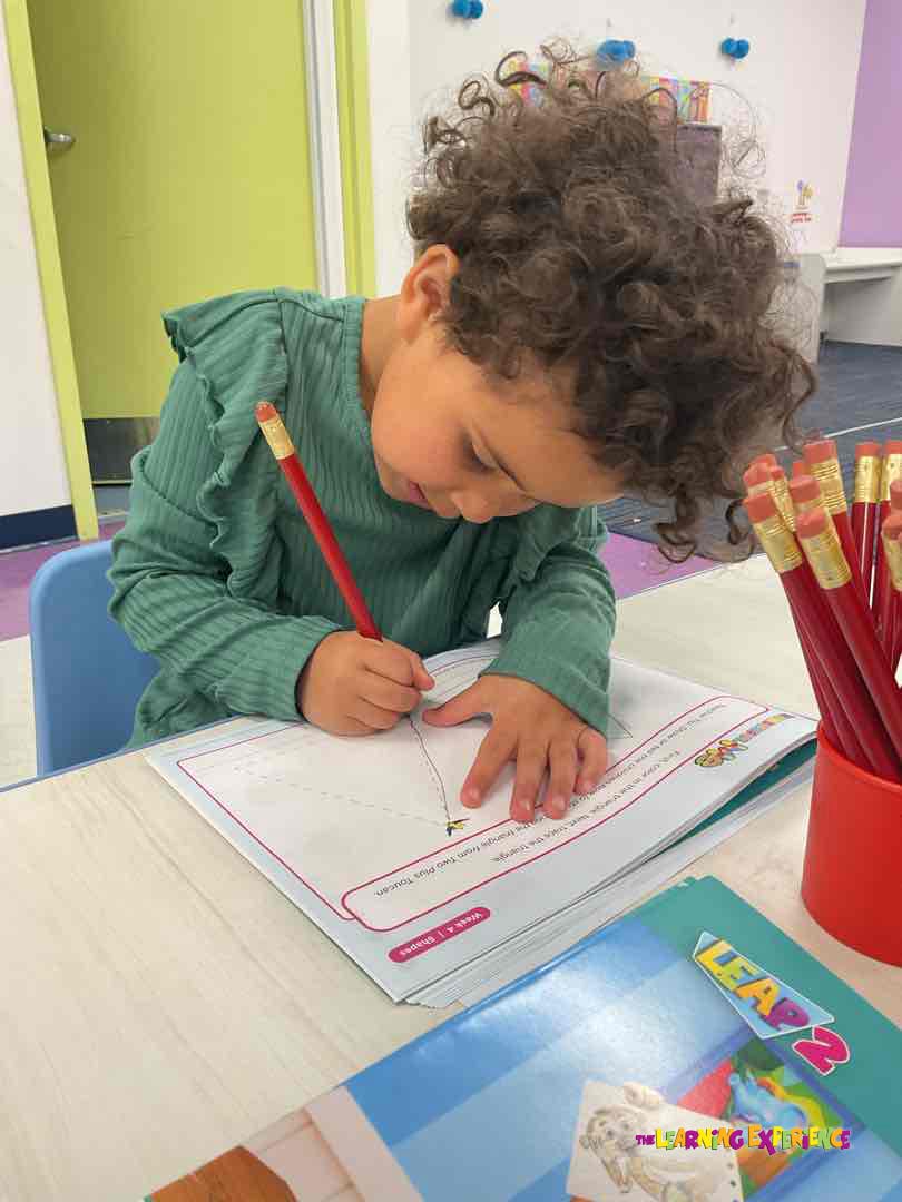 Child with curly hair writing on paper with a red pencil