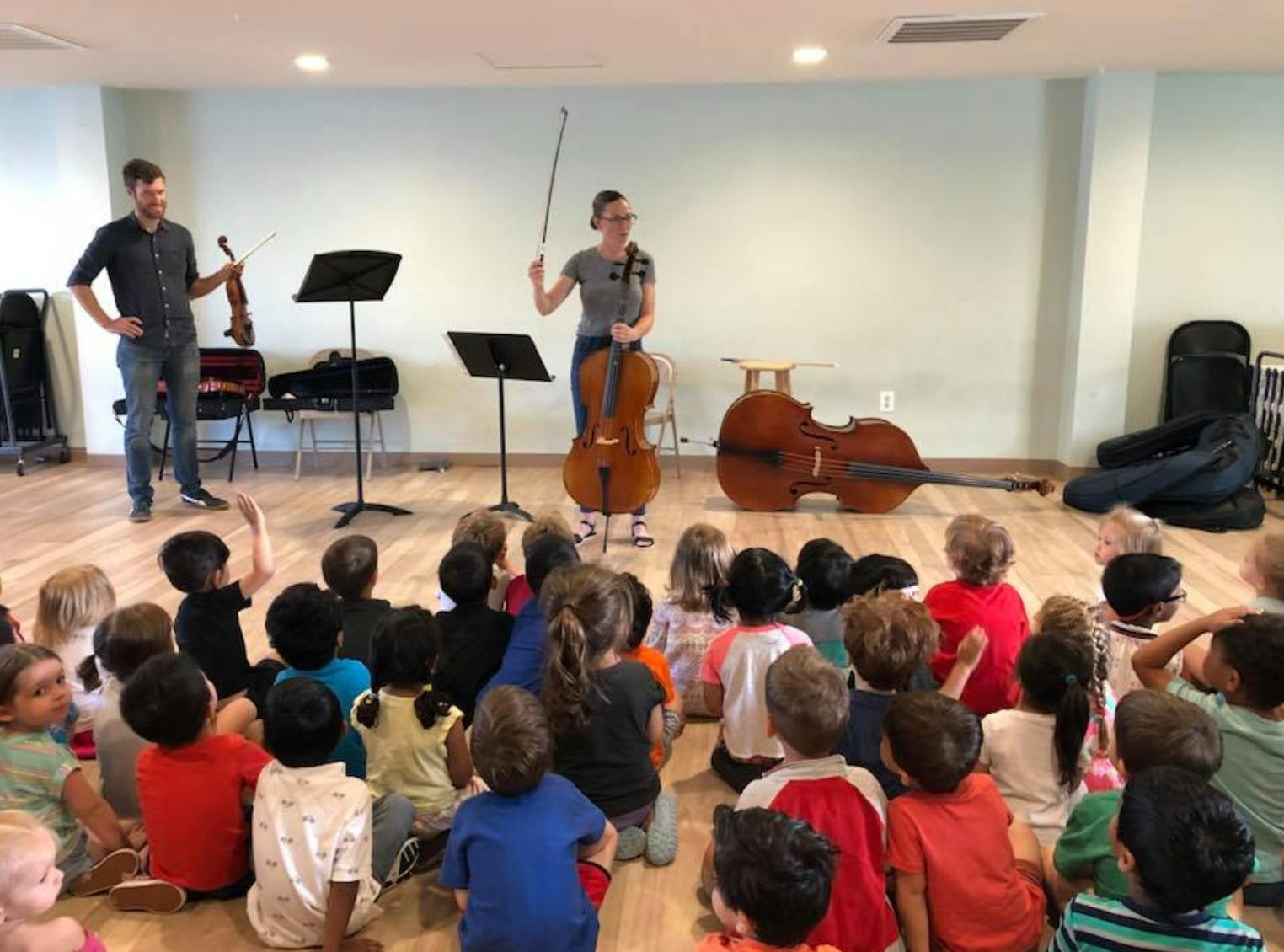 Two people playing string instruments for a group of children