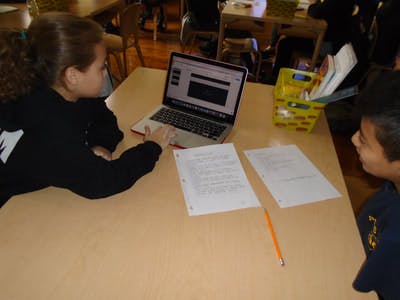 Child using a laptop with another child looking on