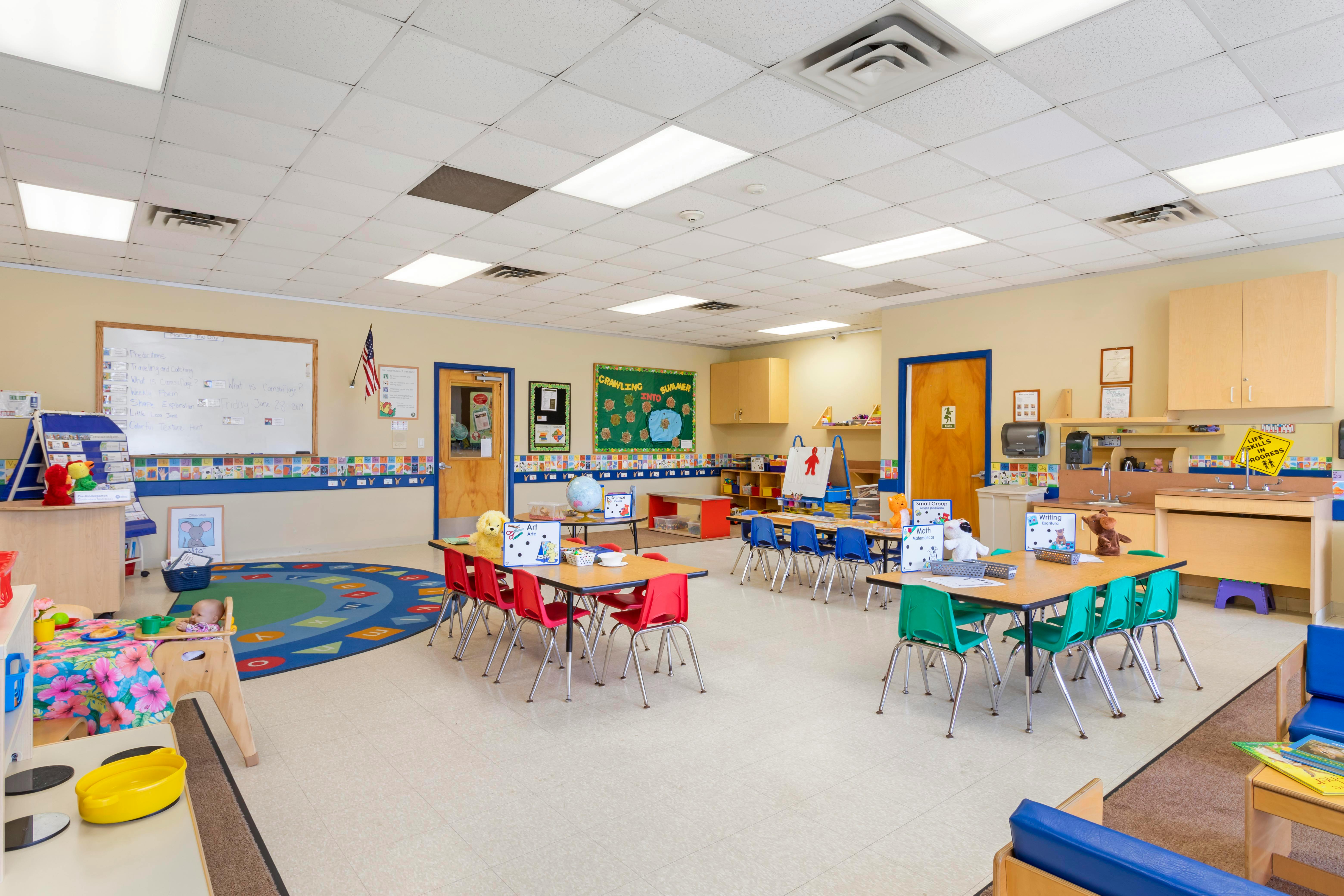 An empty early childhood classroom with colorful tables, chairs, and learning stations