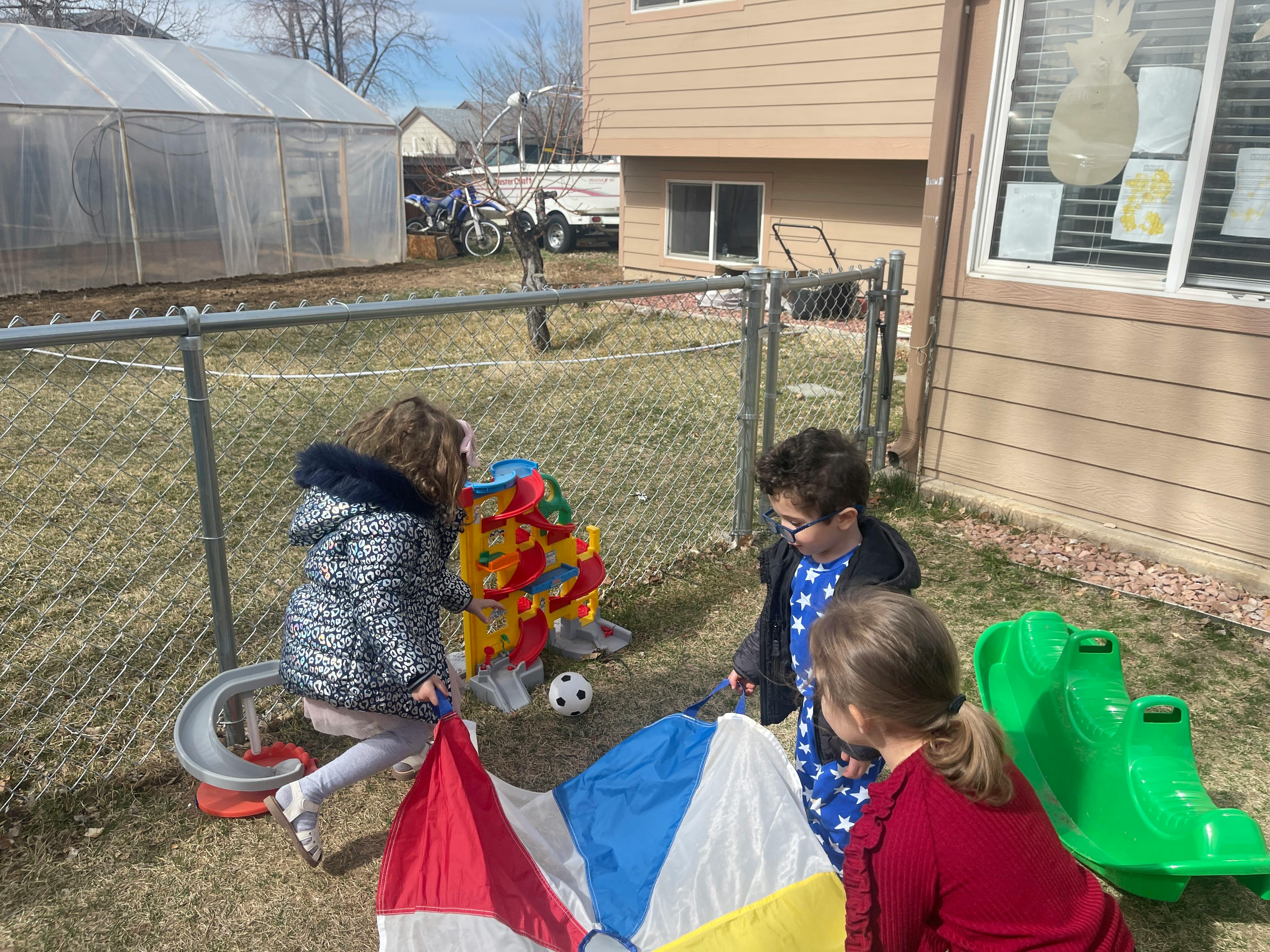 Three children playing outdoors with colorful toys and a parachute