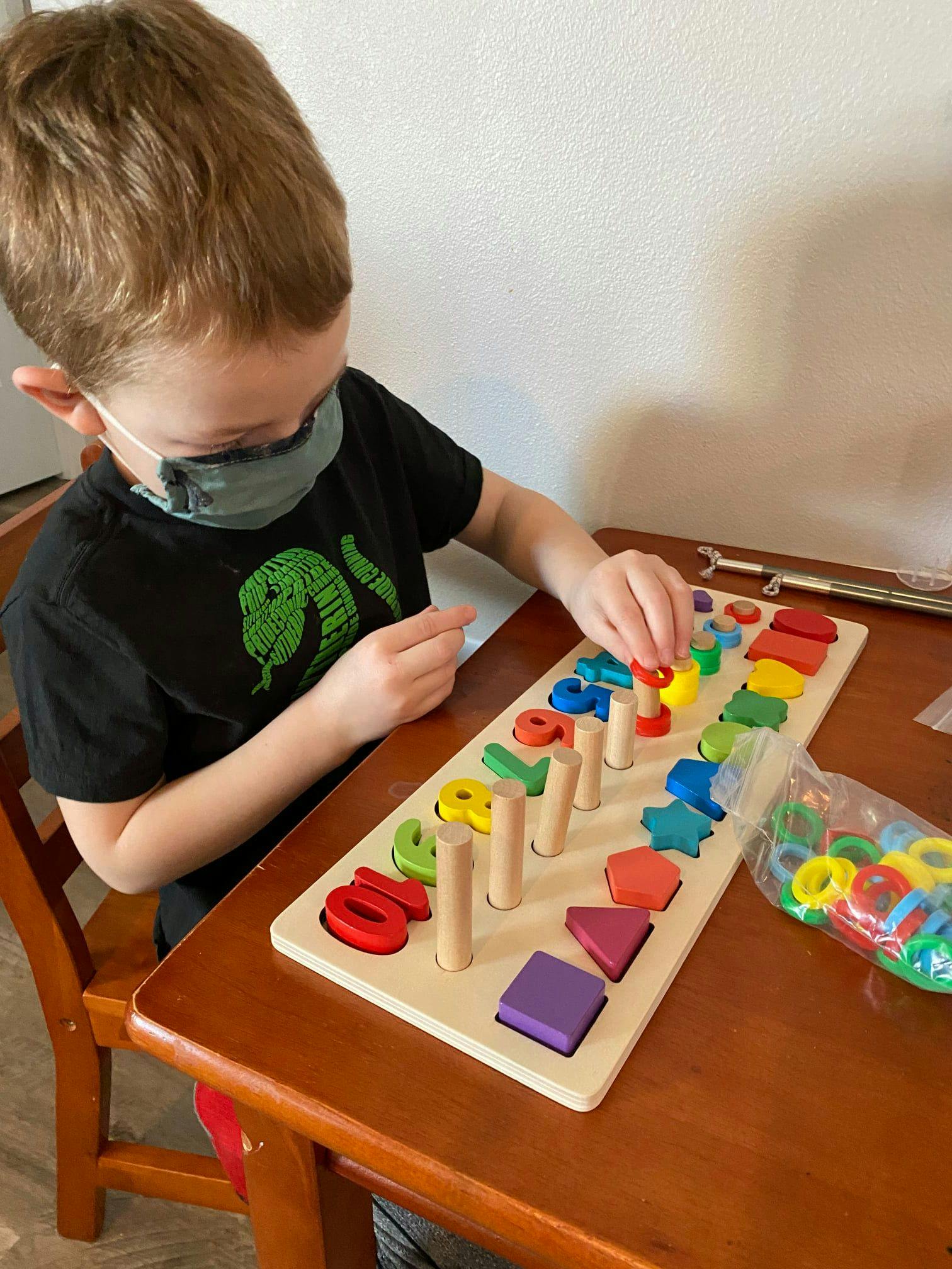 Child in a mask playing with a wooden shape and number puzzle