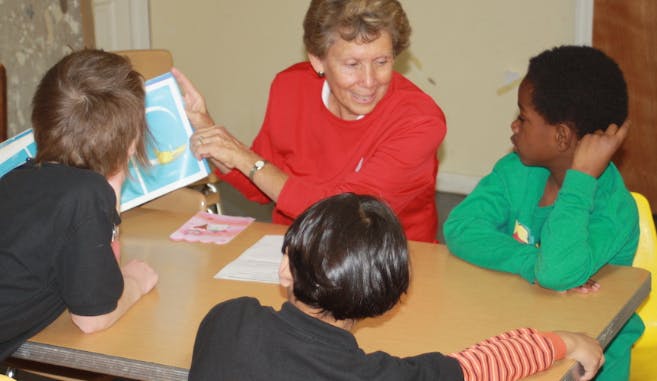 Person showing a book to two children at a table