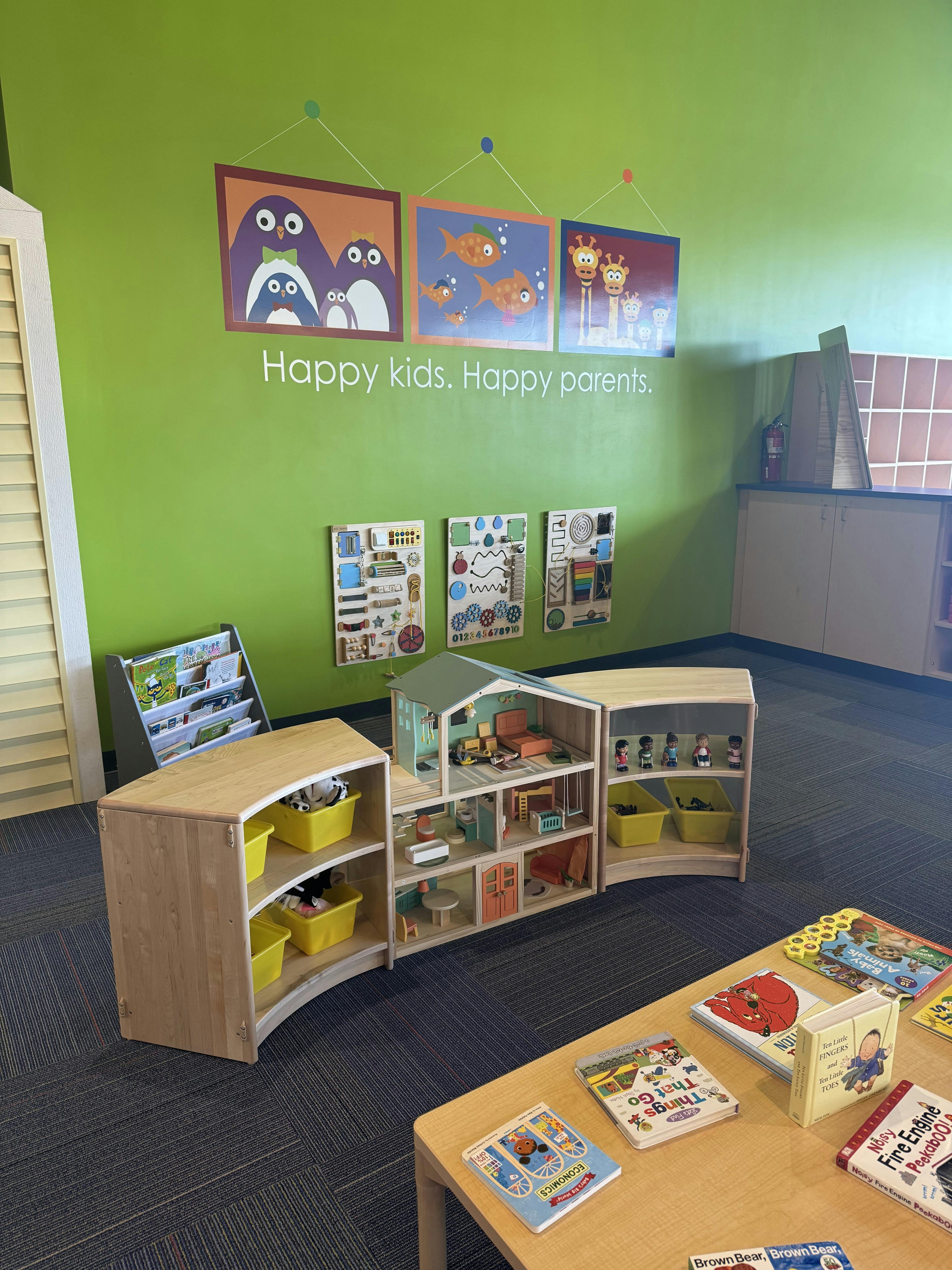 Children's play area with a dollhouse, toy shelves, and books on a table