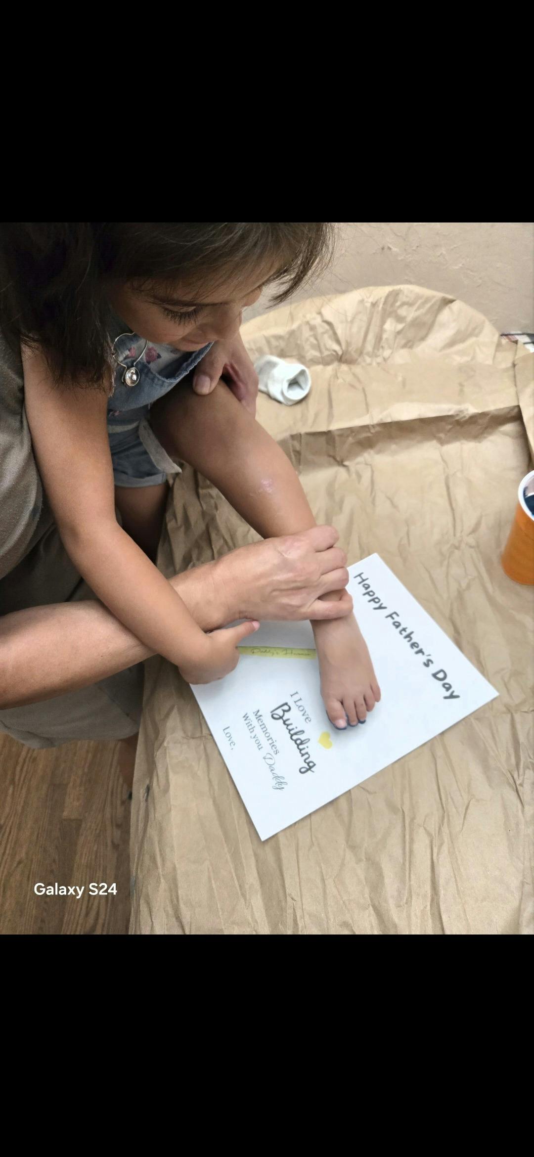 Child pressing foot onto a Happy Father's Day craft paper