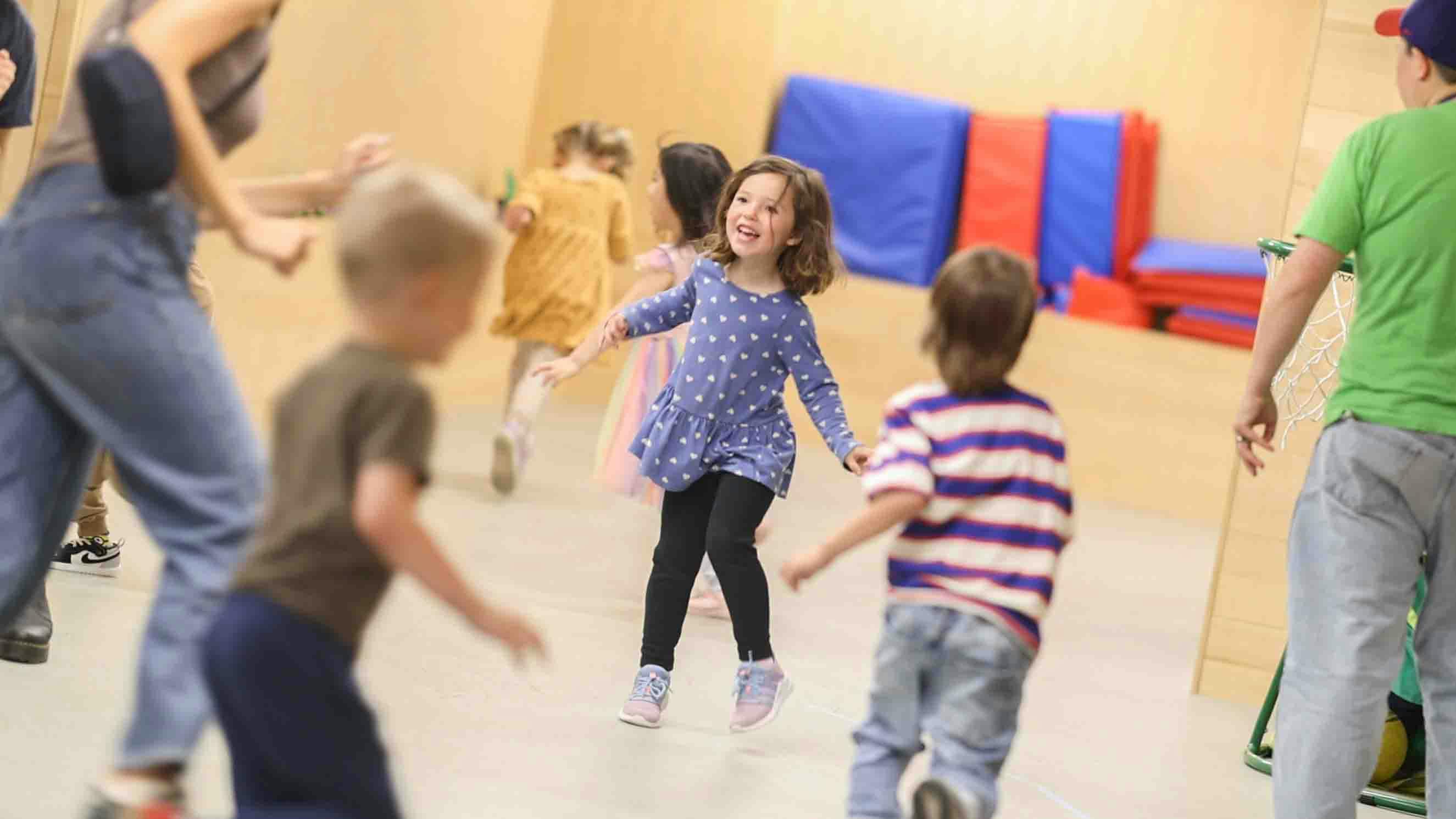 Children running and playing indoors, a girl in a blue dress is smiling