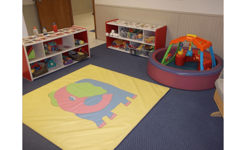 Playroom with toy shelves, a ball pit, and a yellow floor mat with an elephant