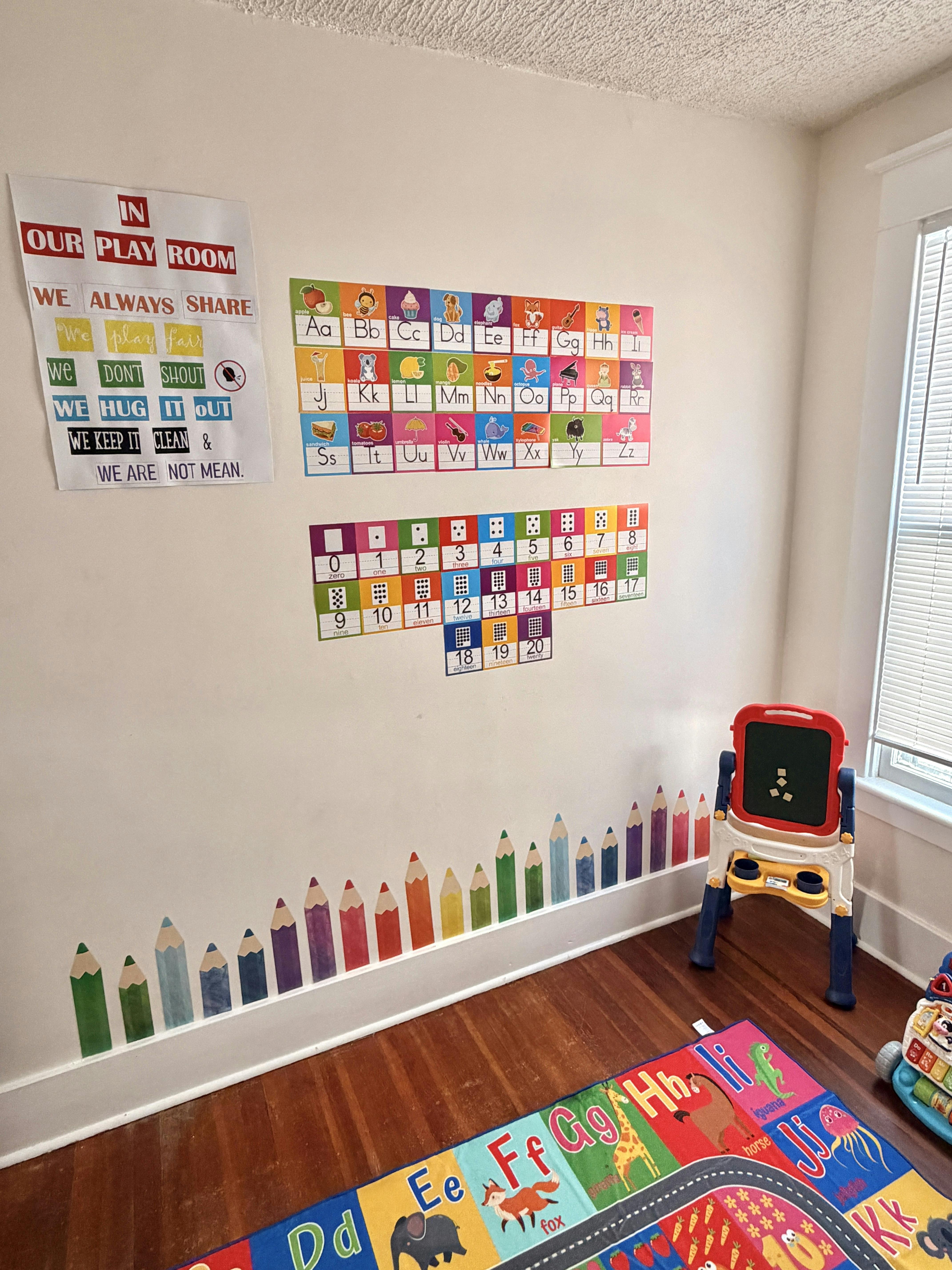 Playroom wall with educational posters, pencil border decals, and a small easel