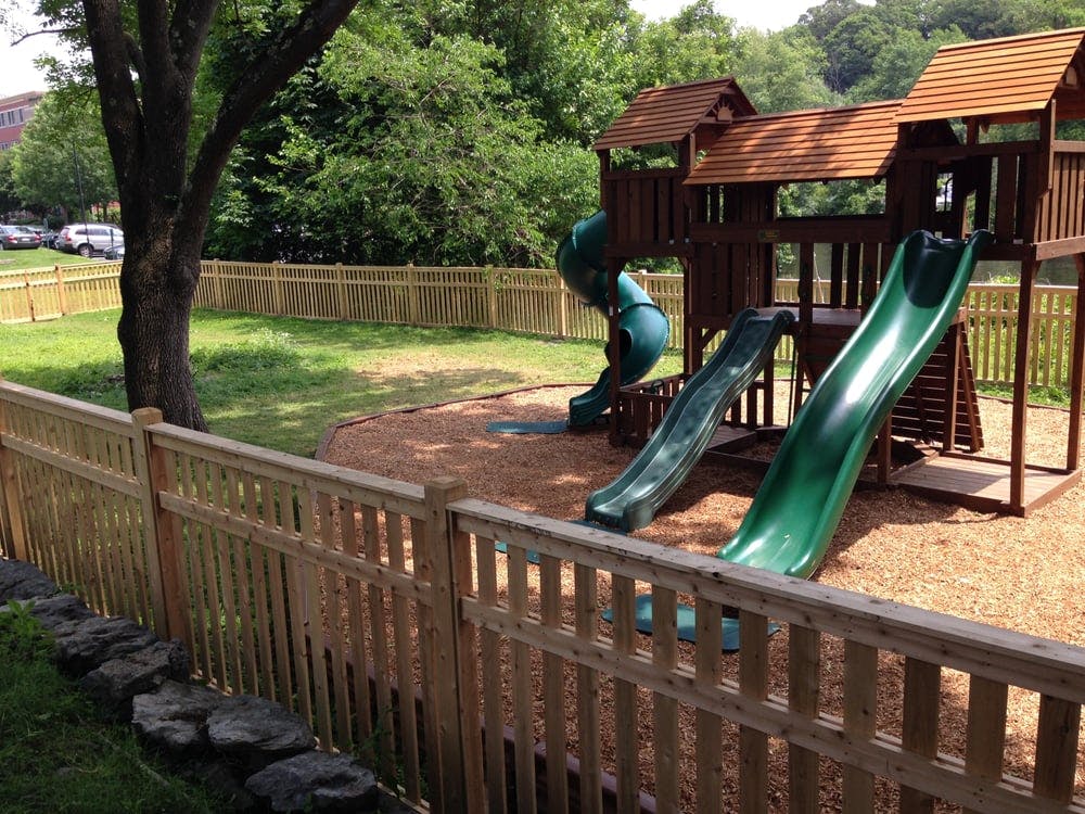 Wooden playground set with green slides and a wooden fence