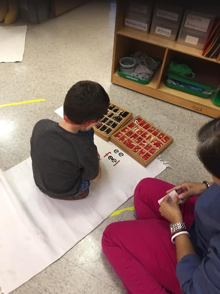 Child and person on floor with letter tiles and paper with "ee feel"