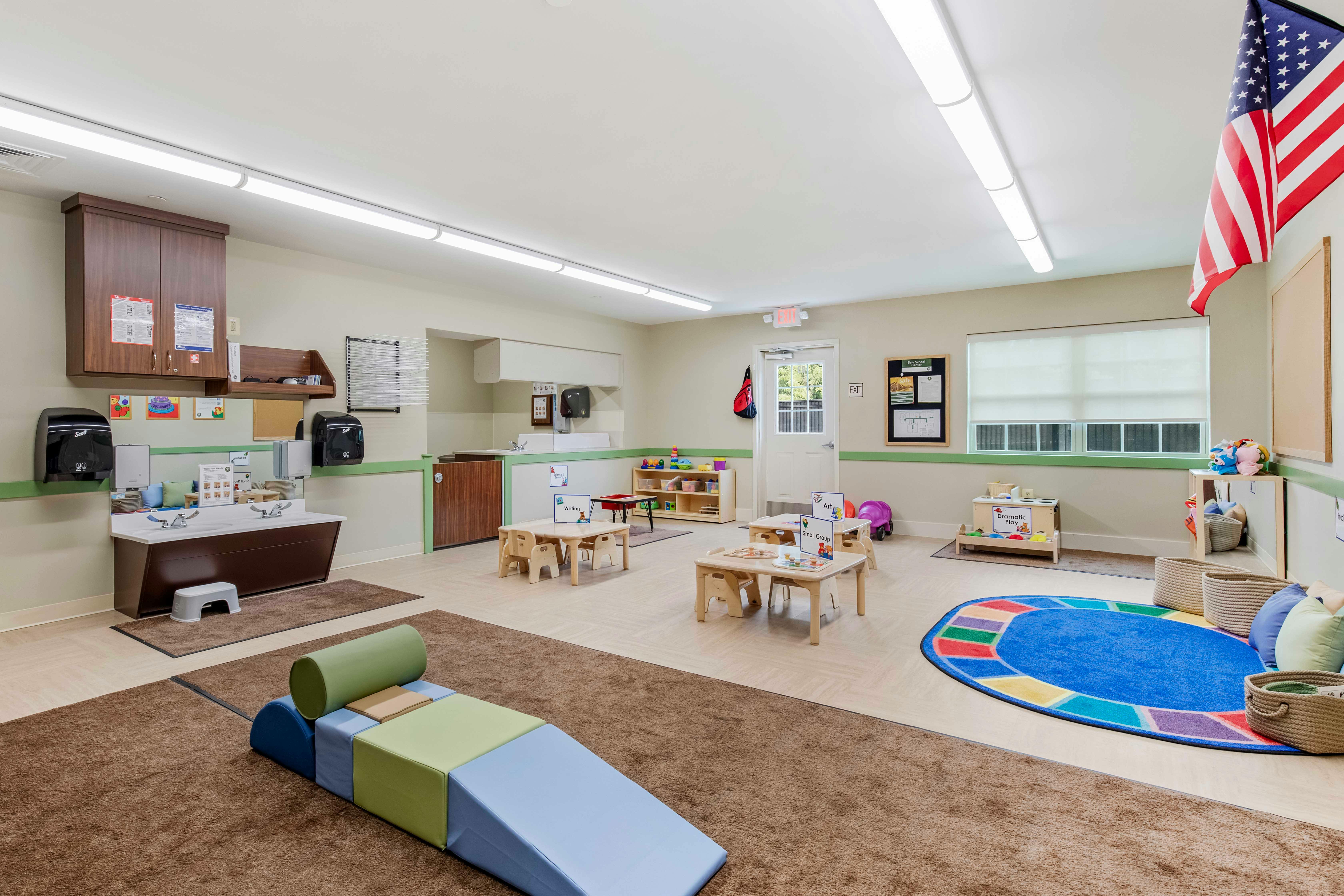 Classroom with child-sized tables, sinks, an American flag, and soft play equipment