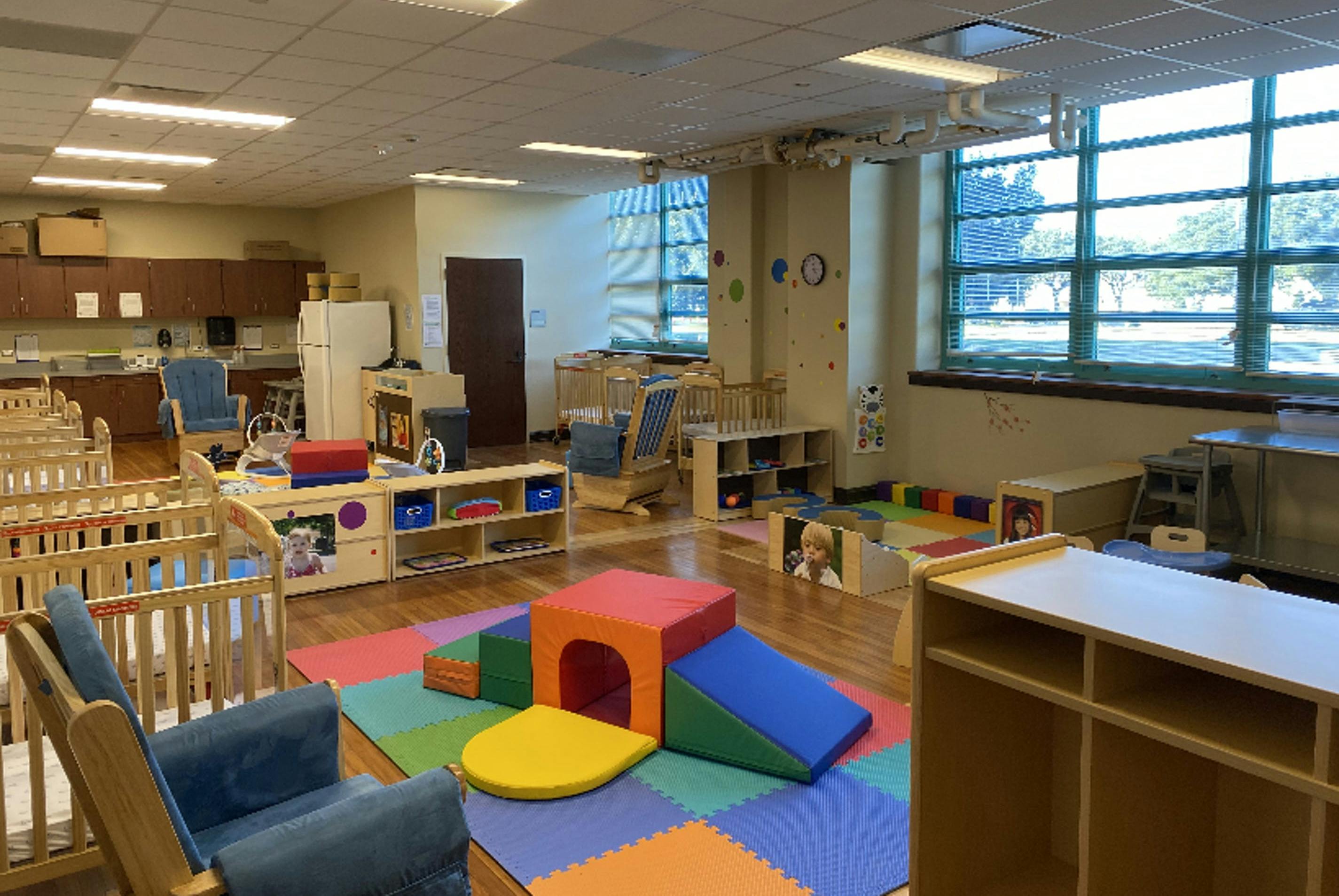 Daycare room with cribs, play mats, and small furniture