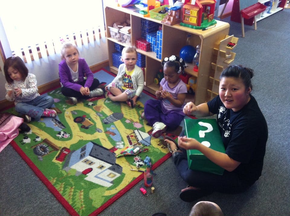 Person and children sitting on a rug in a classroom