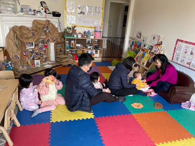 People and children sitting on colorful floor mats in a classroom