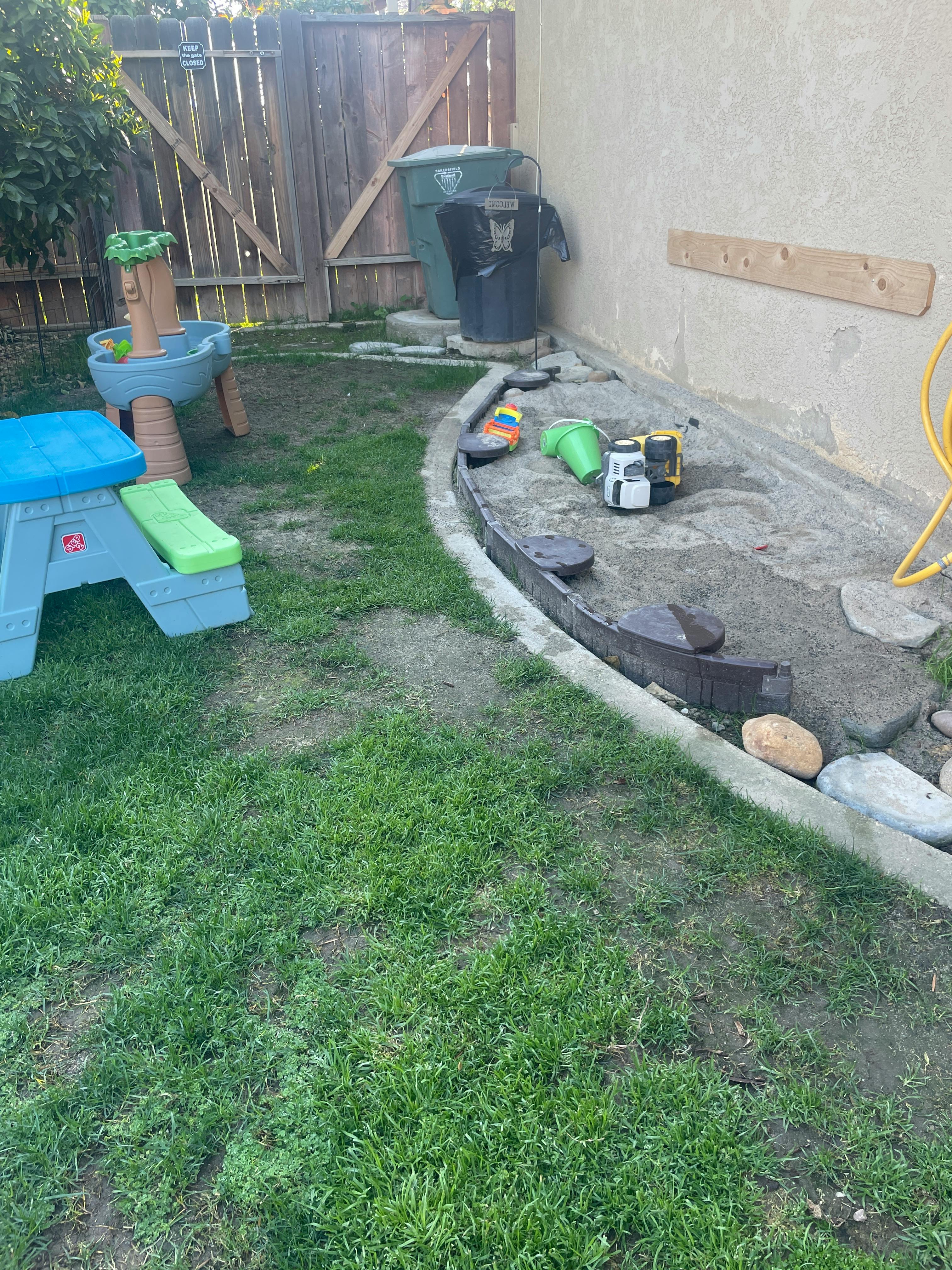 Backyard with a small picnic table, water table, and toys in a planter