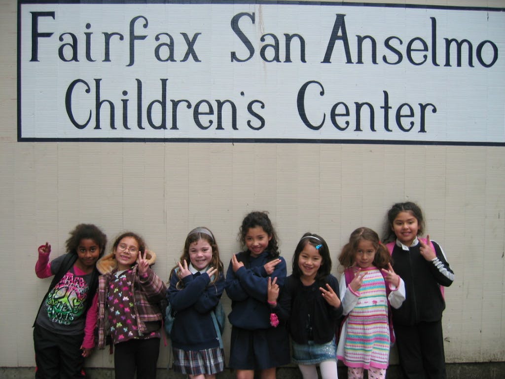 Seven children standing in front of a sign for a children's center
