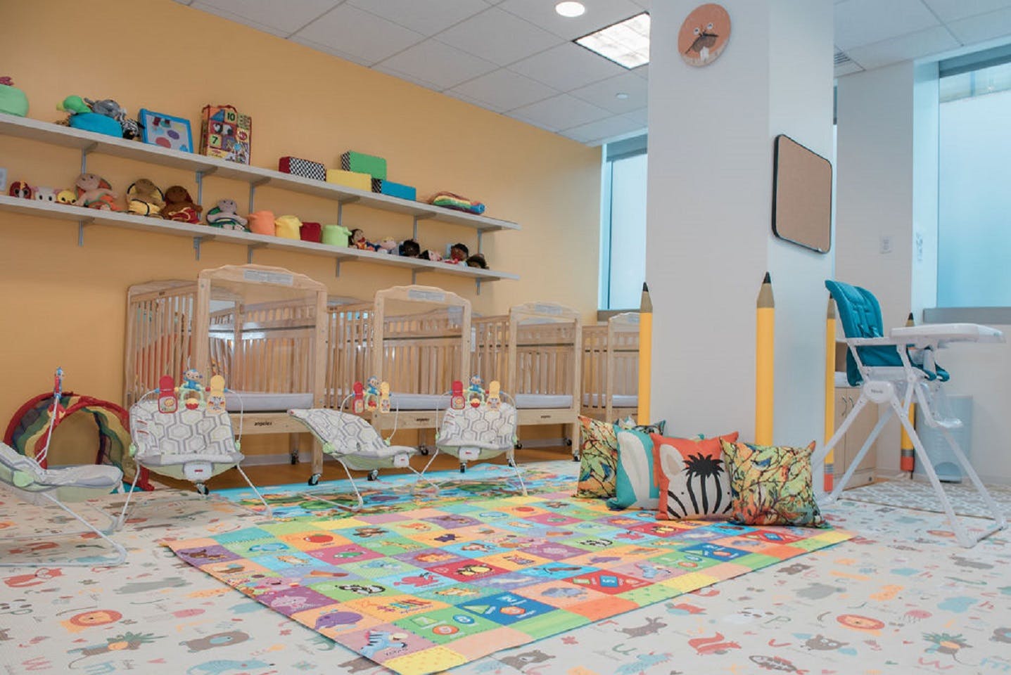 Cribs, infant seats, play mats, and a high chair in a childcare room