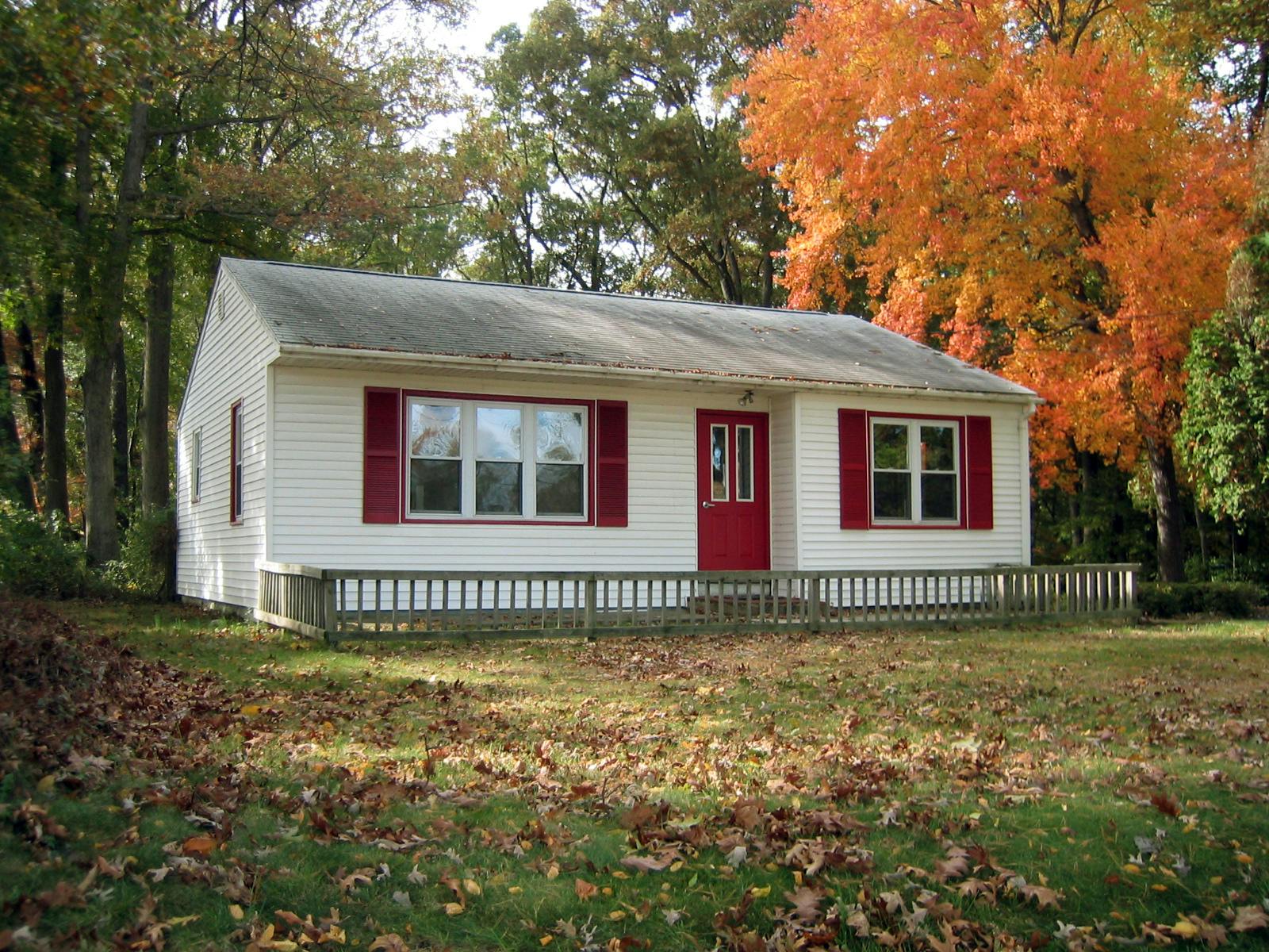 White house with red door and shutters, autumn trees in background