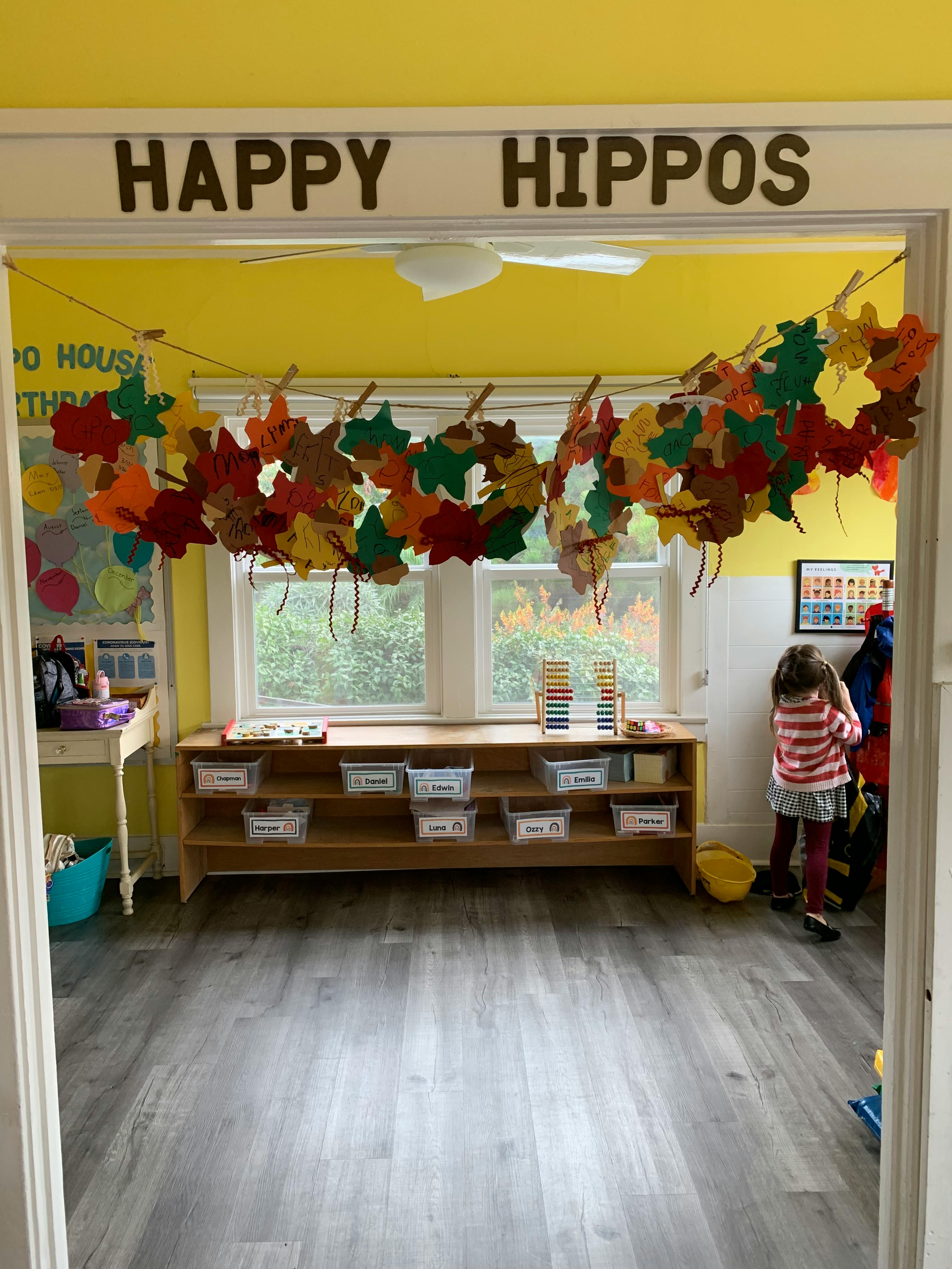 Child in a classroom with "HAPPY HIPPOS" sign and leaf garland