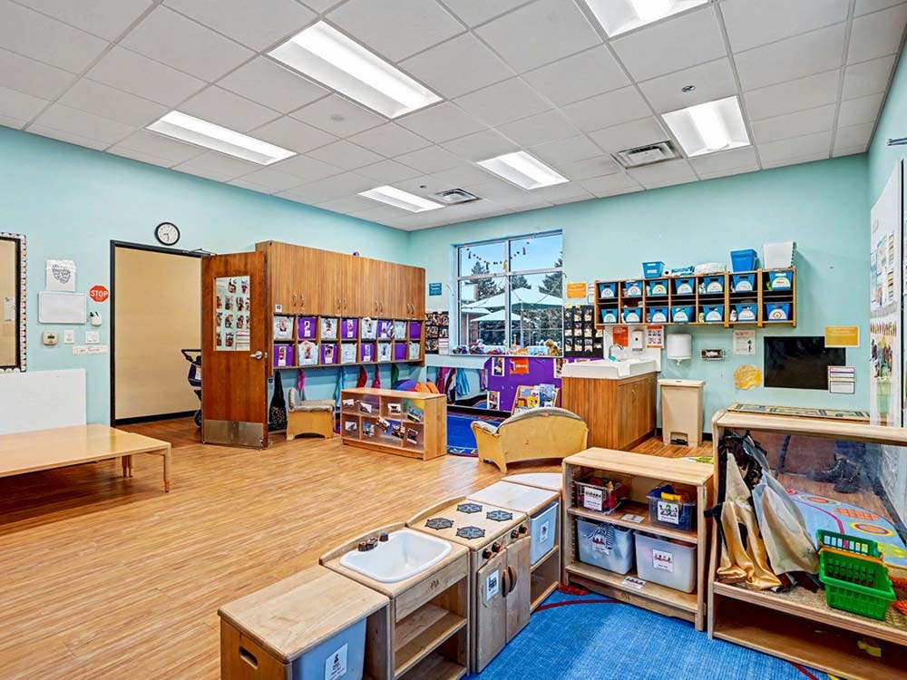 Classroom with children's furniture, shelves, and a window overlooking an outdoor area