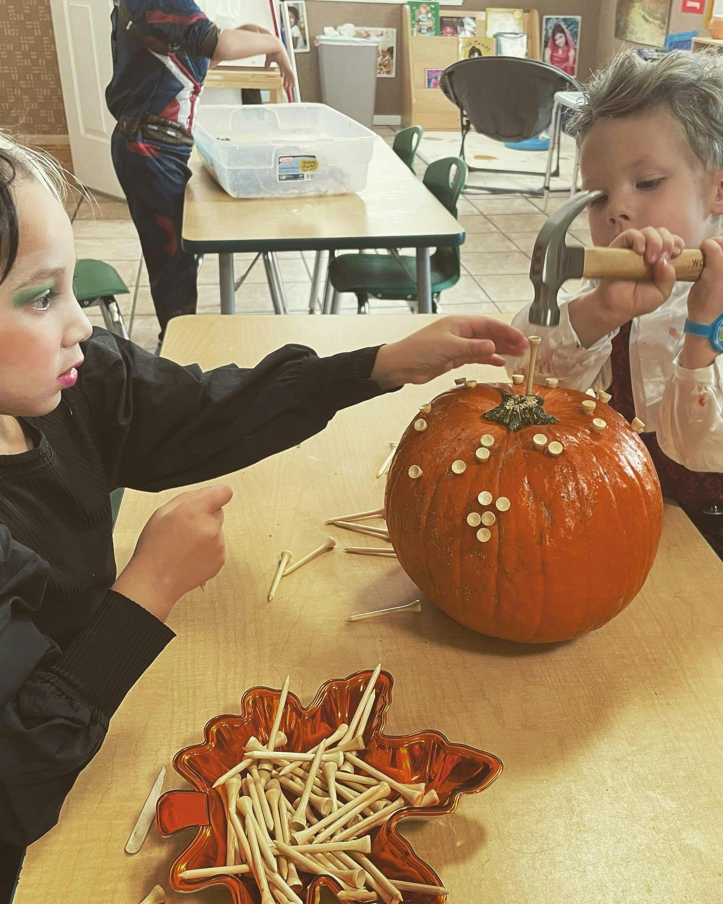 Two children decorating a pumpkin with golf tees and a hammer