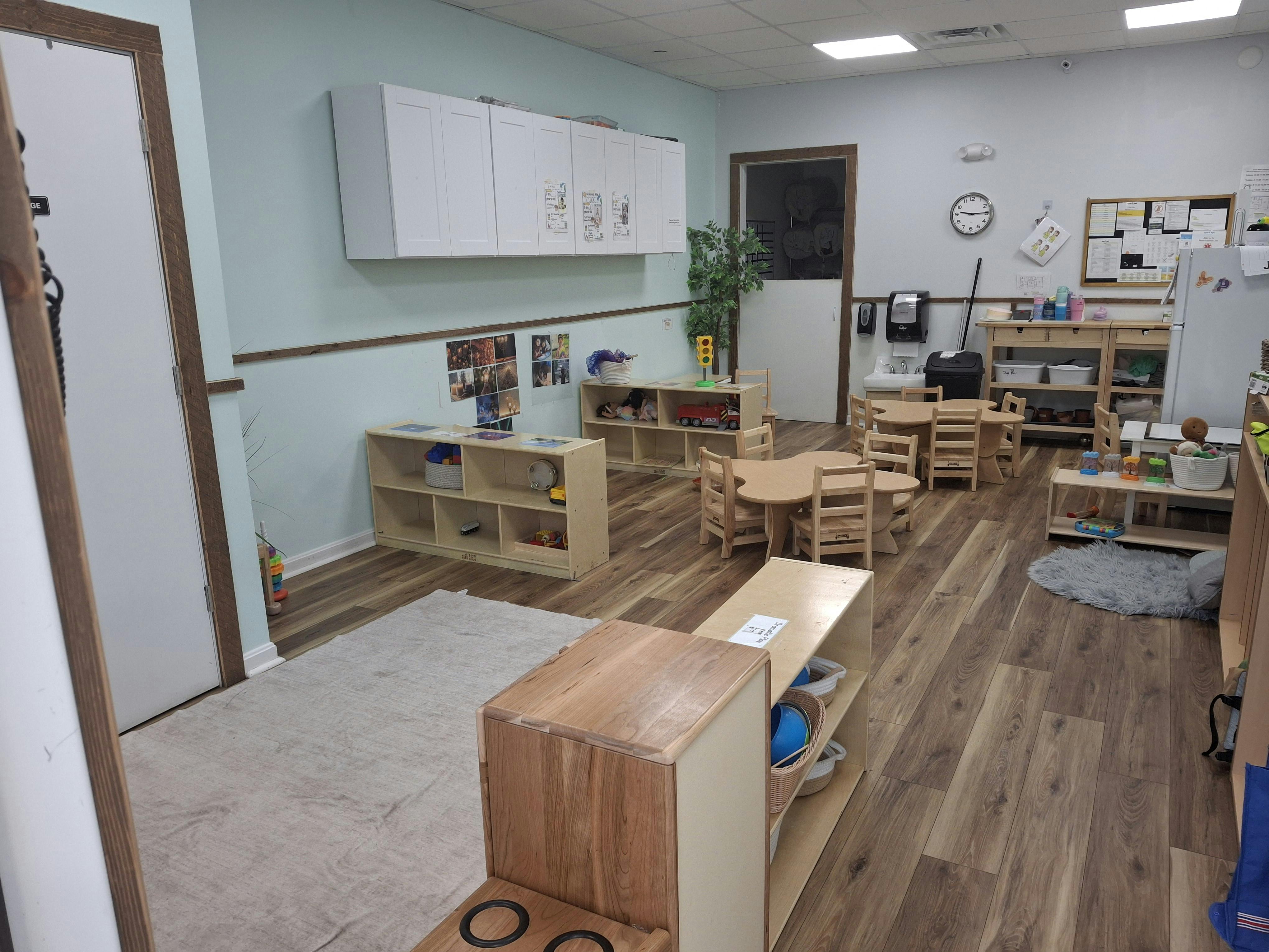 Classroom with small wooden tables and chairs, shelves, and a rug