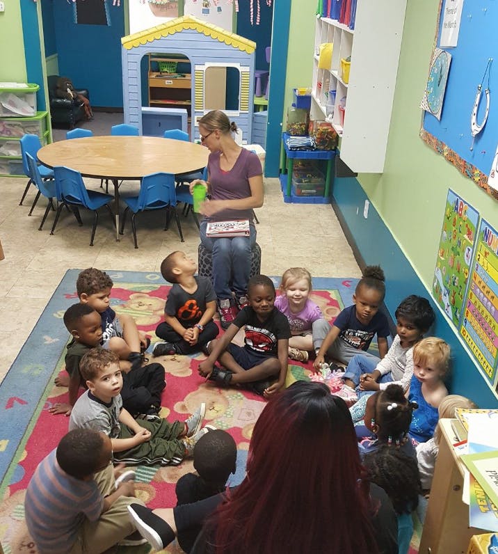 Adult reading to a group of children sitting on a rug in a classroom