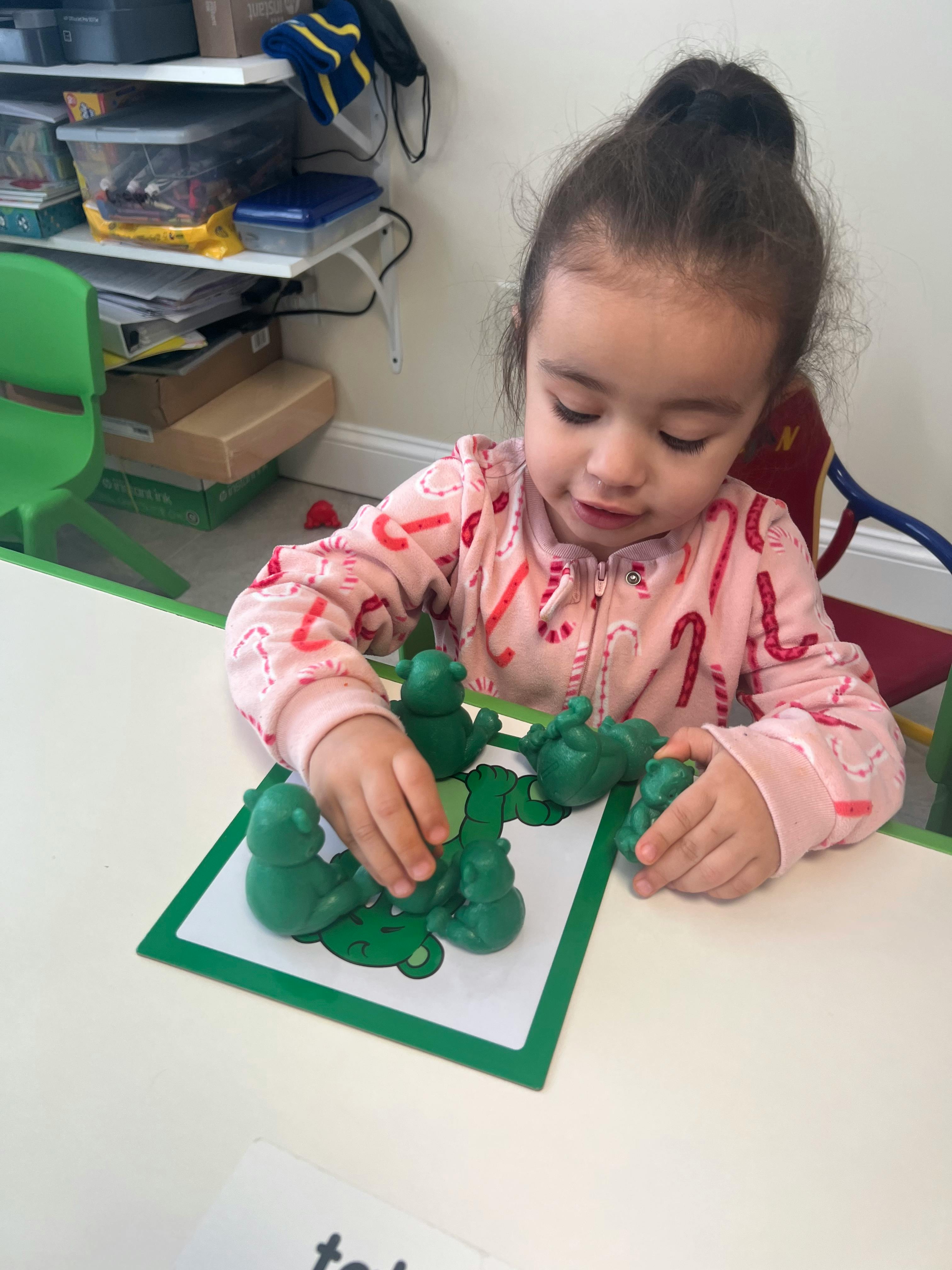 Child playing with green playdough on a white table