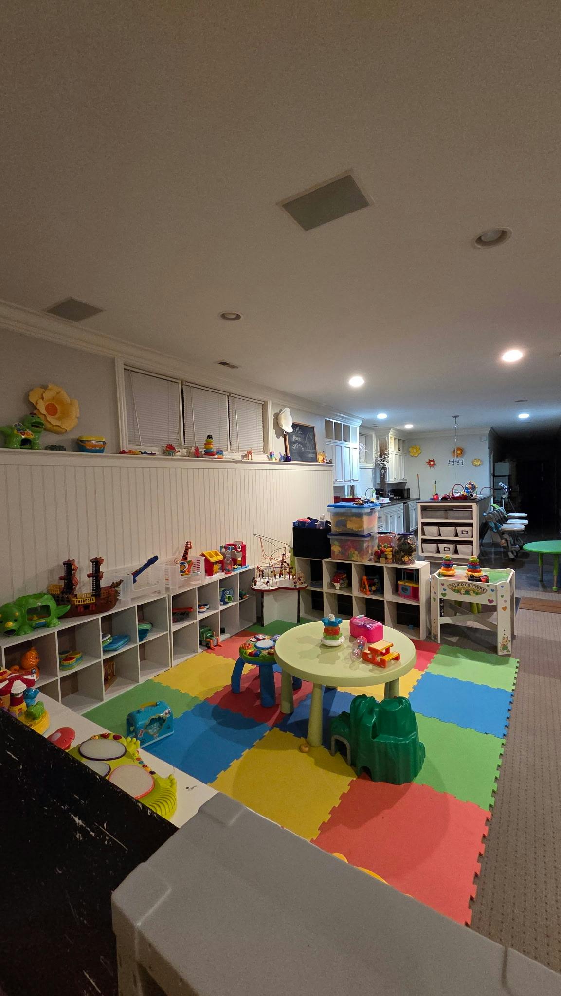 Playroom with colorful floor mats, shelves of toys, and a small table